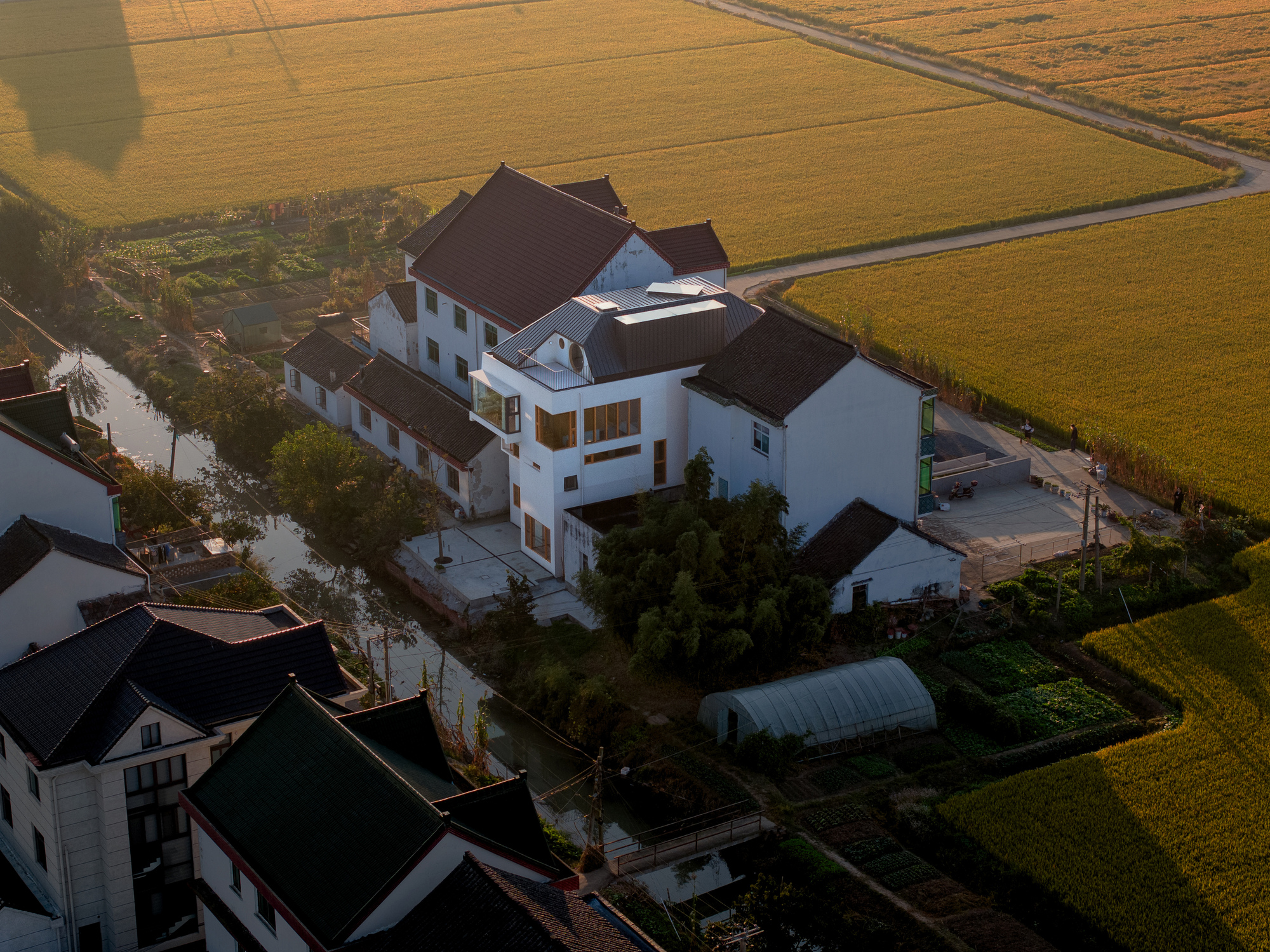 Aerial view at sunset showing the clustered white volumes and pitched roofs surrounded by farmland and waterways