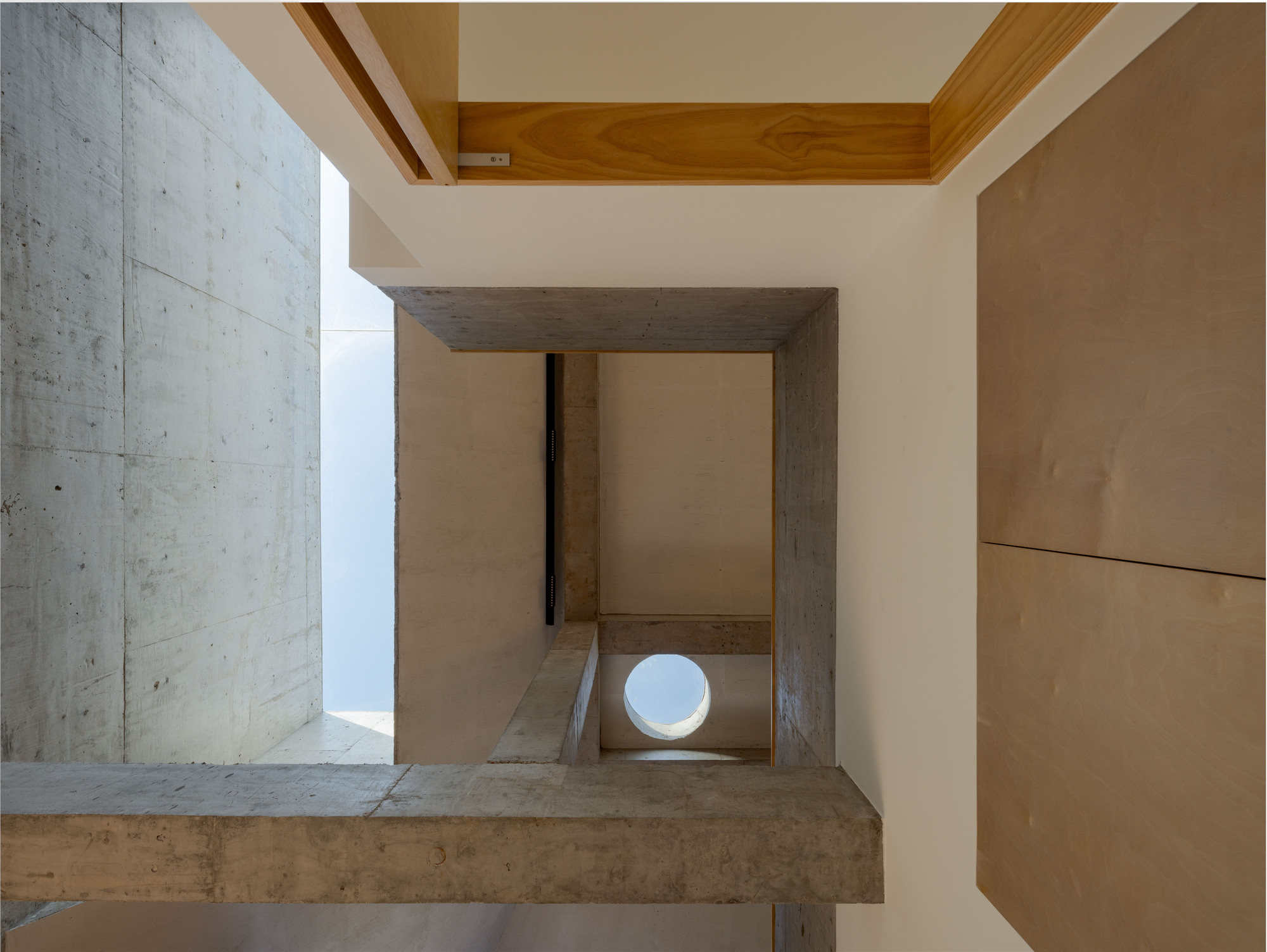 View down through a concrete frame opening showing timber stairs and a circular window below