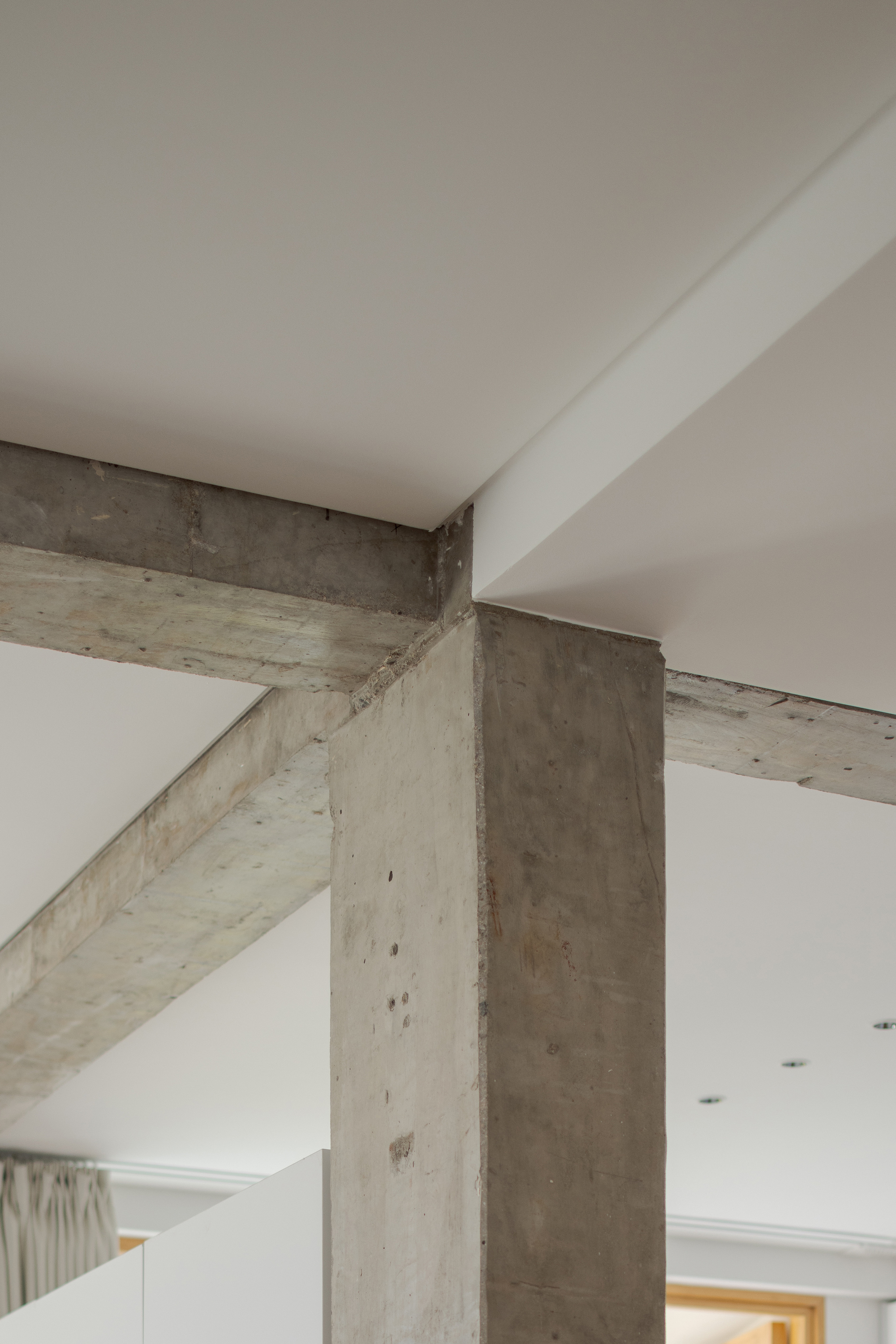 Close-up of exposed concrete beams and column intersecting white ceiling planes at multiple angles