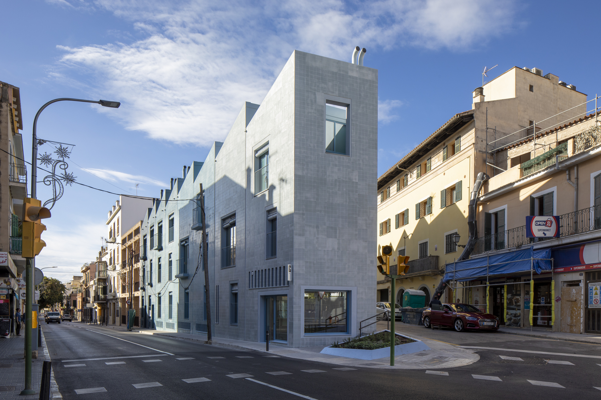 Corner facade clad in white tile facing a street intersection in afternoon light