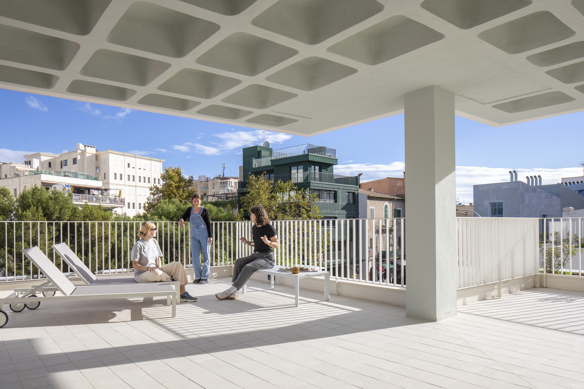 Rooftop terrace with coffered concrete ceiling and white vertical railing under midday sun