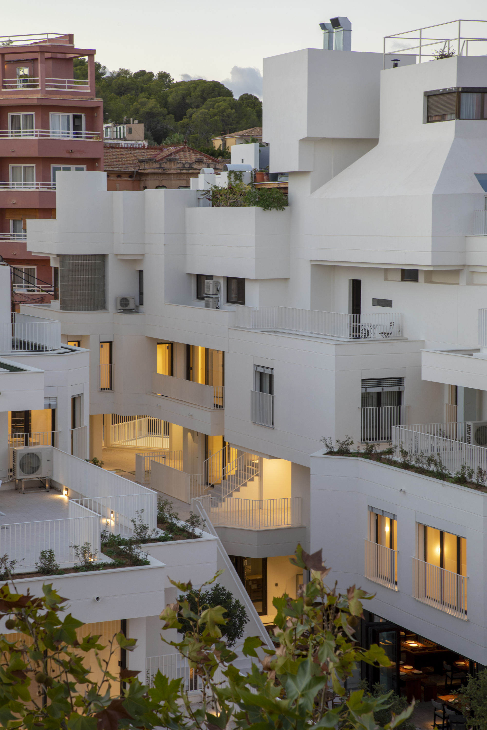Stacked white volumes with planted terraces and warm interior lighting at twilight