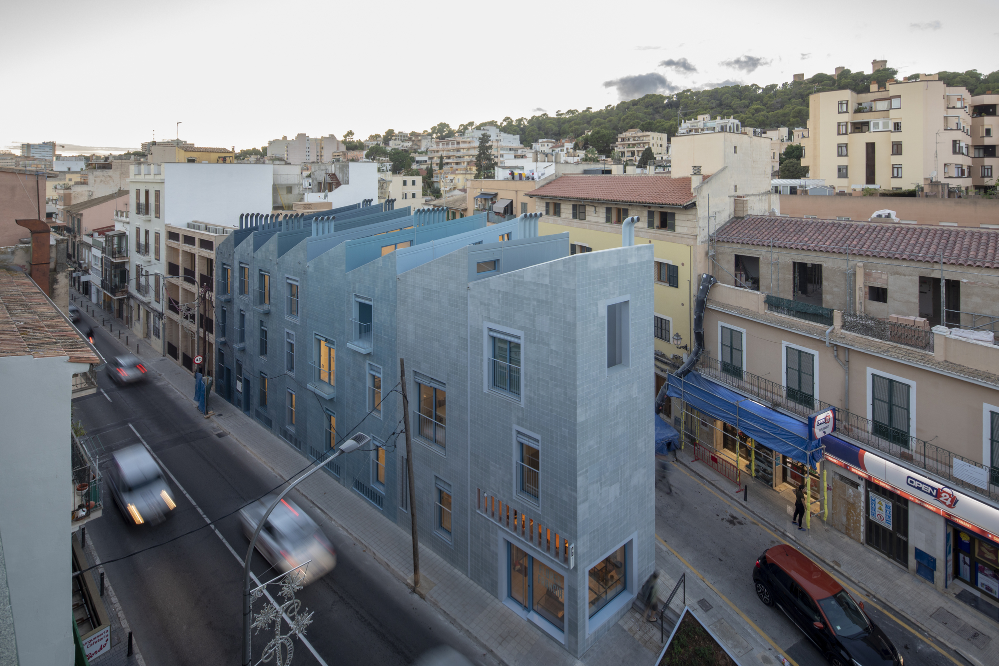 Gridded tile facade on a corner building with moving traffic and pedestrians at dusk