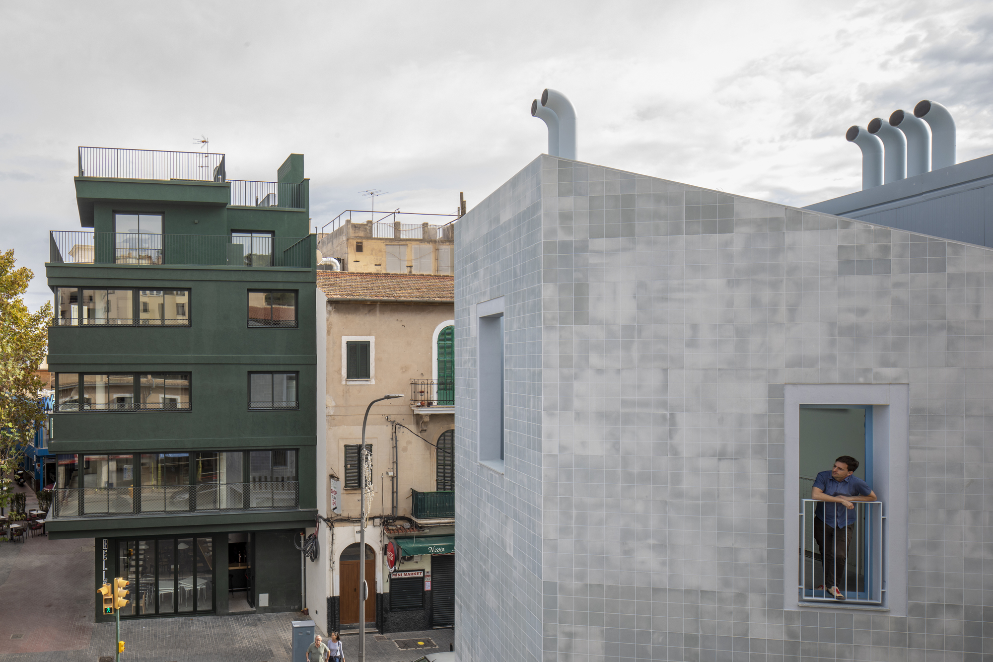 Tiled facade with recessed balcony window occupied by a person under cloudy skies