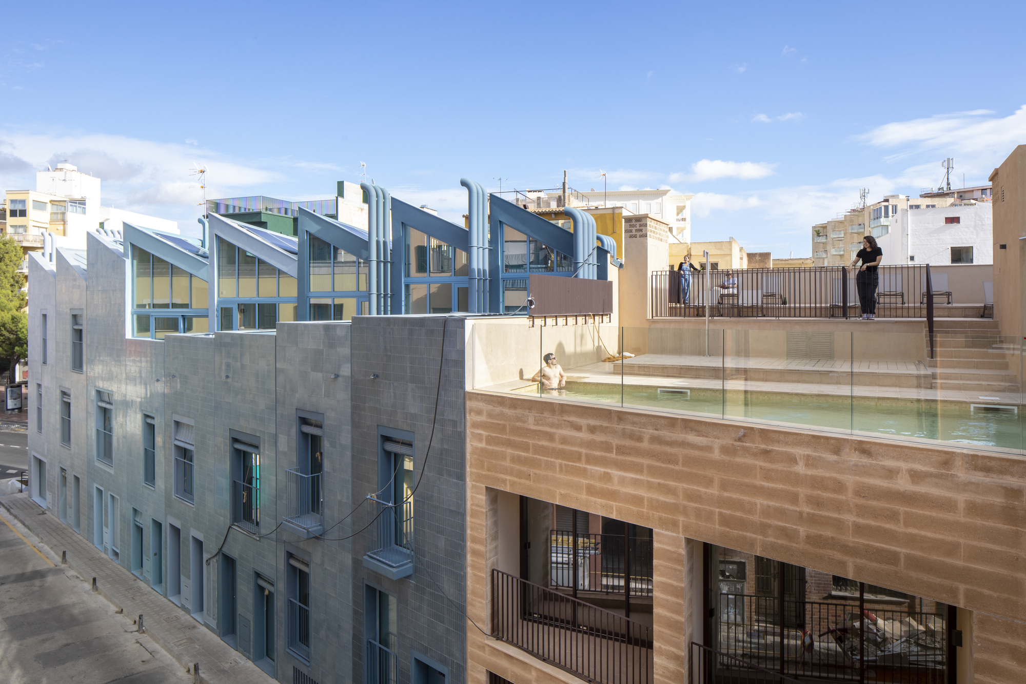 Rooftop terrace with glass railings and swimming pool overlooking sawtooth glazed volumes under afternoon light