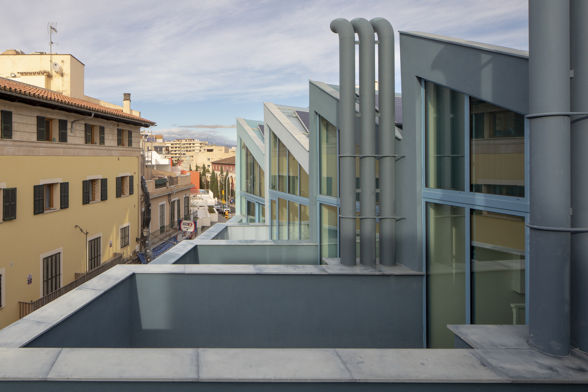 Rooftop terrace showing three industrial ducts and angled glass pavilions against a cloudy sky