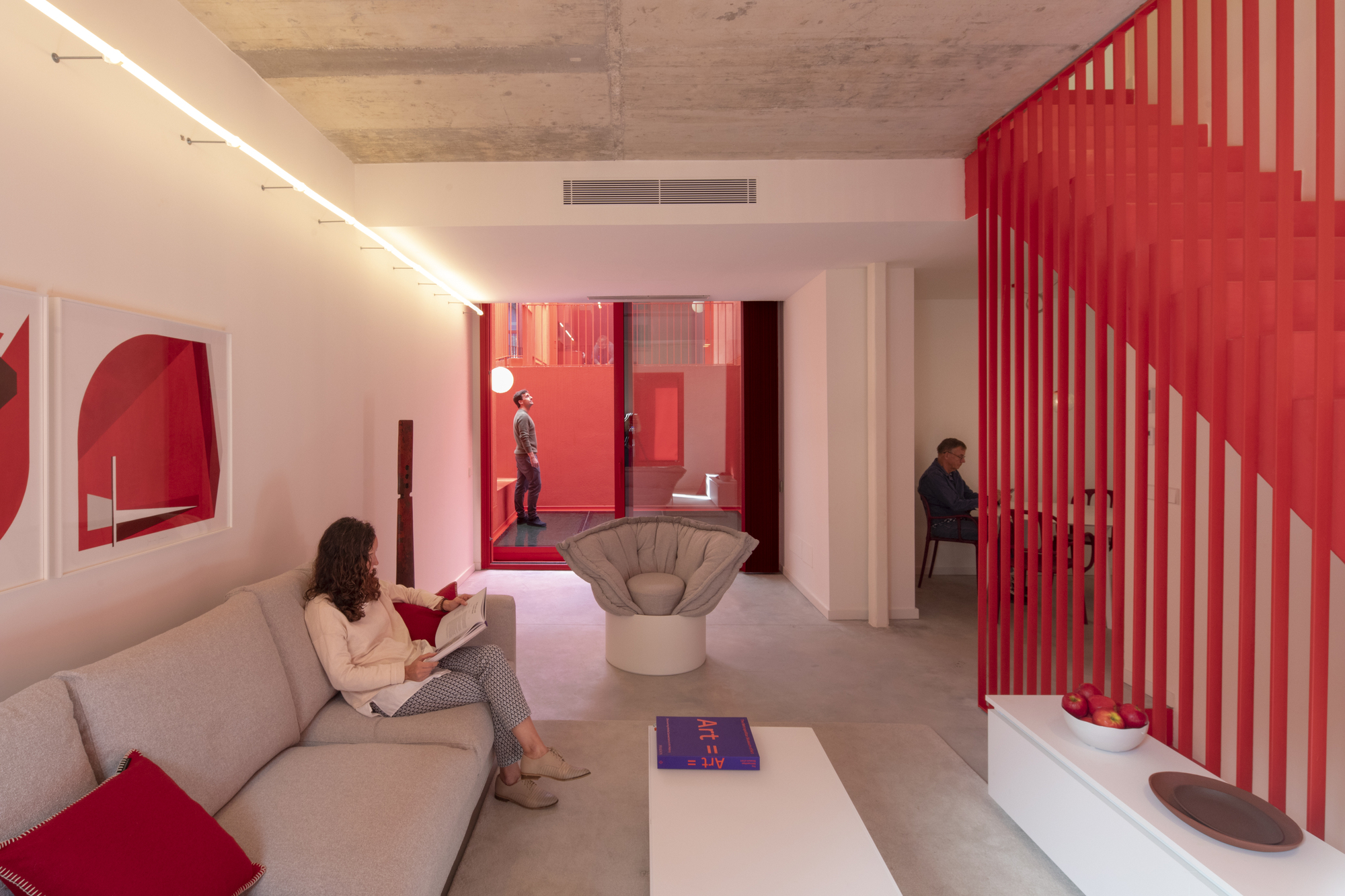 Interior with red slatted staircase screen and view through glazed courtyard where two people stand