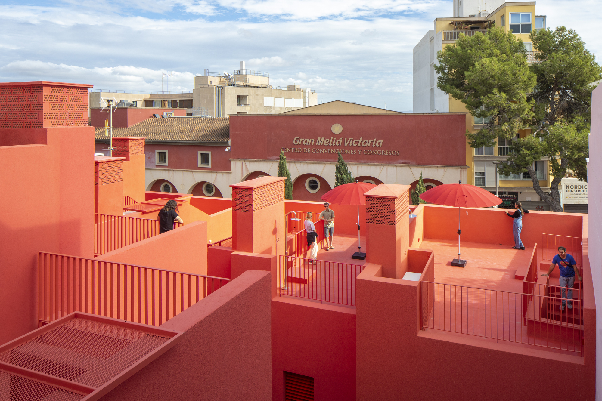 Rooftop platforms in red and orange with corrugated metal screens and visitors under cloudy sky