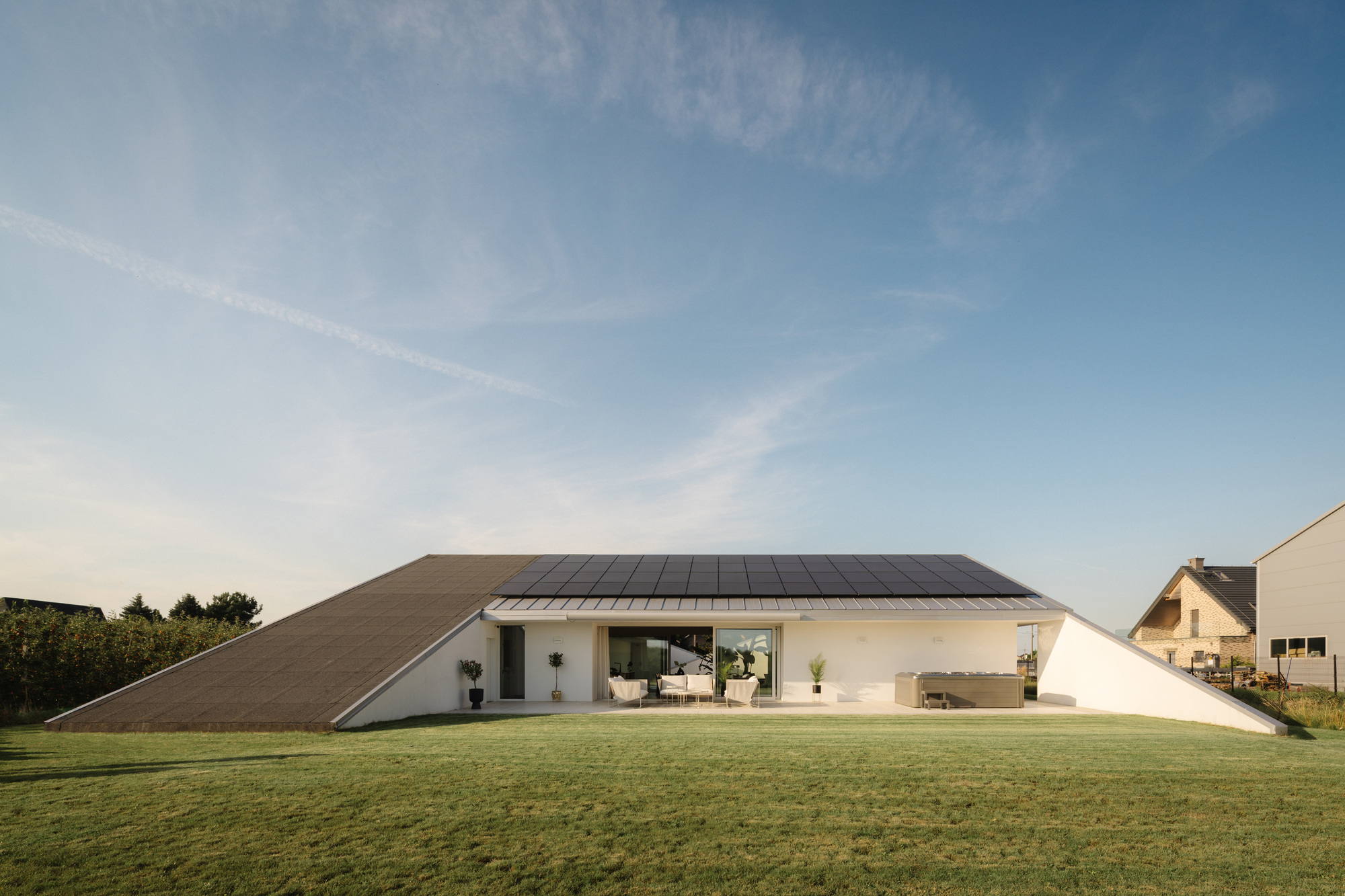Sloped roof with solar panels rising from a white rendered facade across a manicured lawn at dusk
