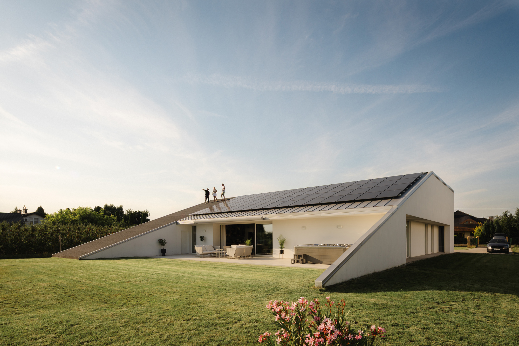 Sloped roof with standing figures and covered terrace opening to lawn with flowering shrub