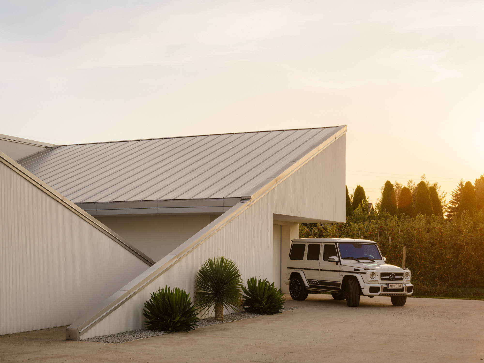 Entry courtyard with standing seam metal roof planes and vehicle parked at dusk