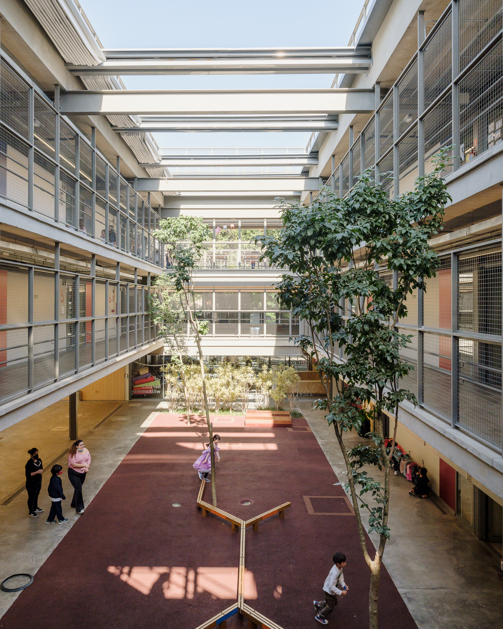 Long view down the internal courtyard with planted trees casting shadows on the maroon floor surface