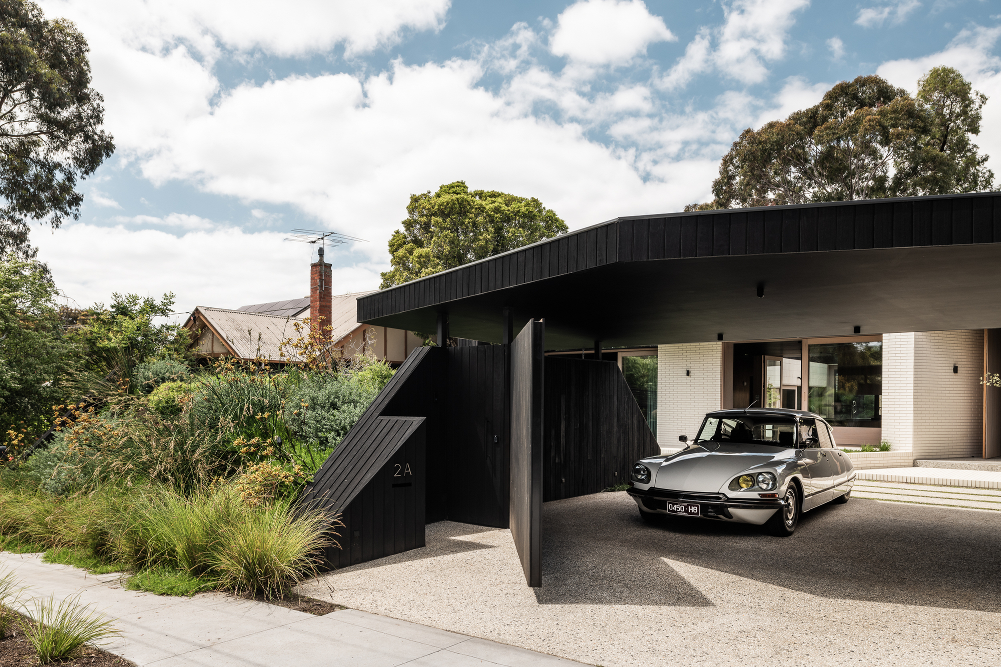 Carport with angled black timber cladding and a vintage sedan parked beneath the sweeping roof overhang