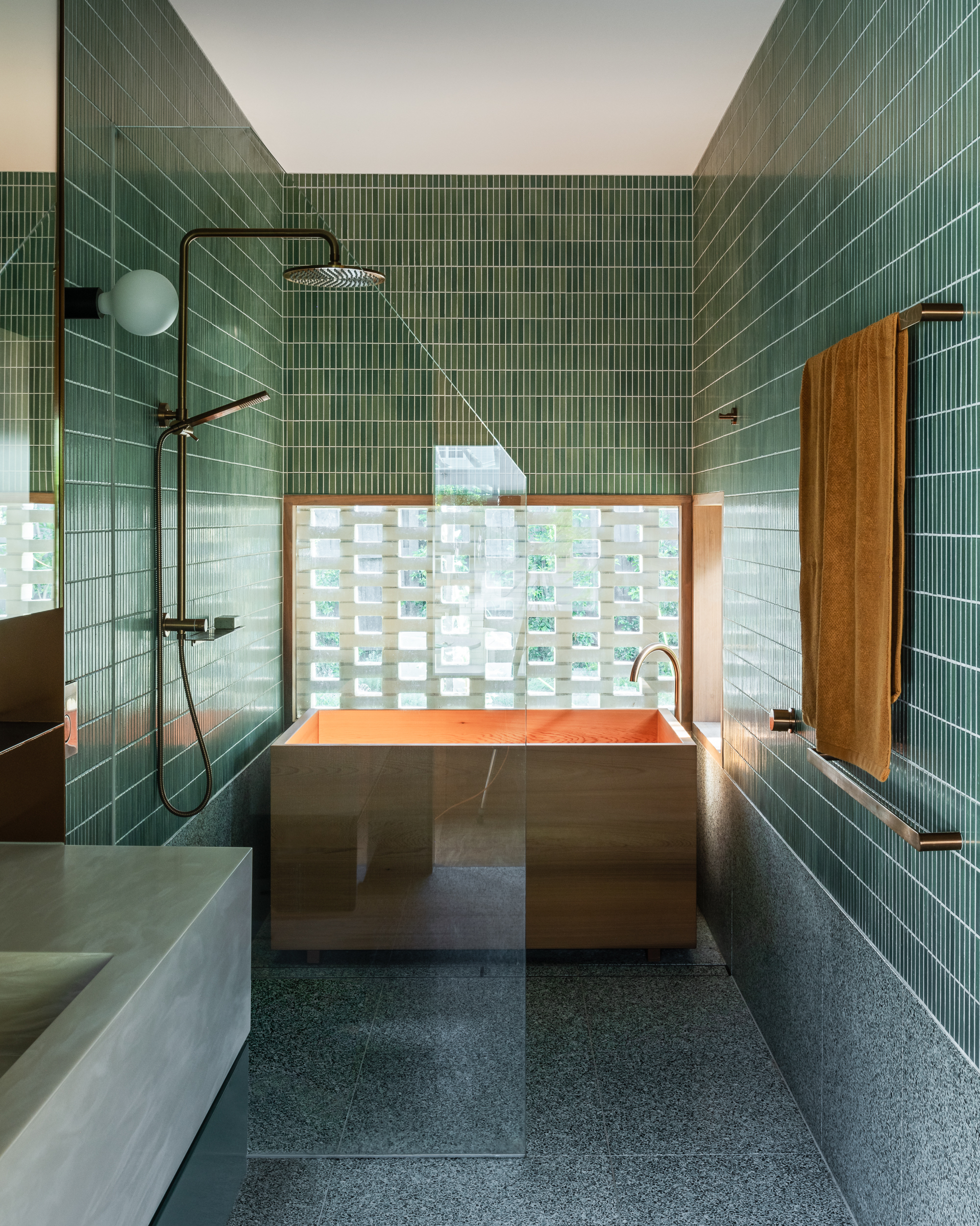 Bathroom with green vertical tile walls, copper bathtub and a translucent glass block window behind