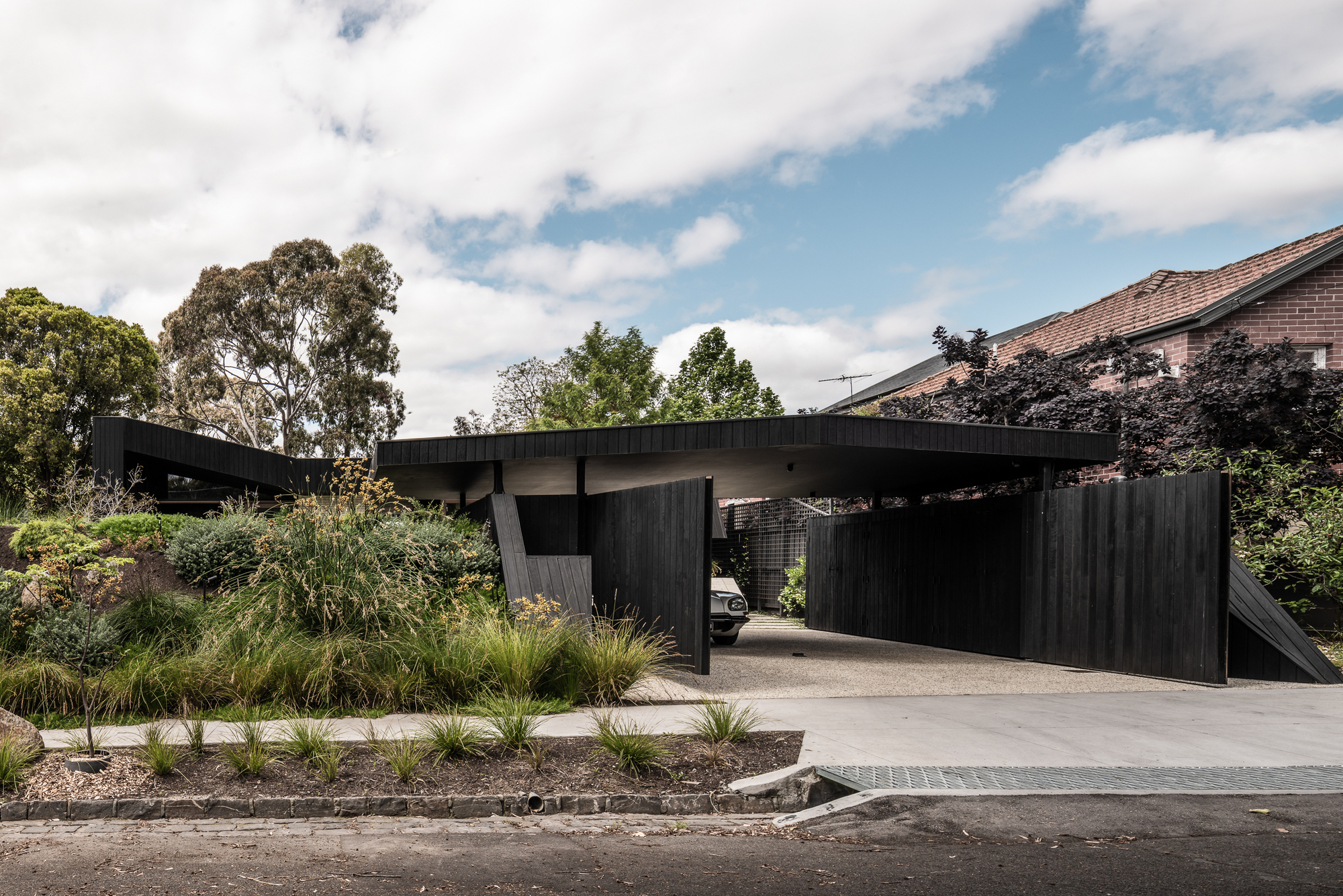 Street view of the cantilevered carport with vertical timber cladding and native grasses along the driveway