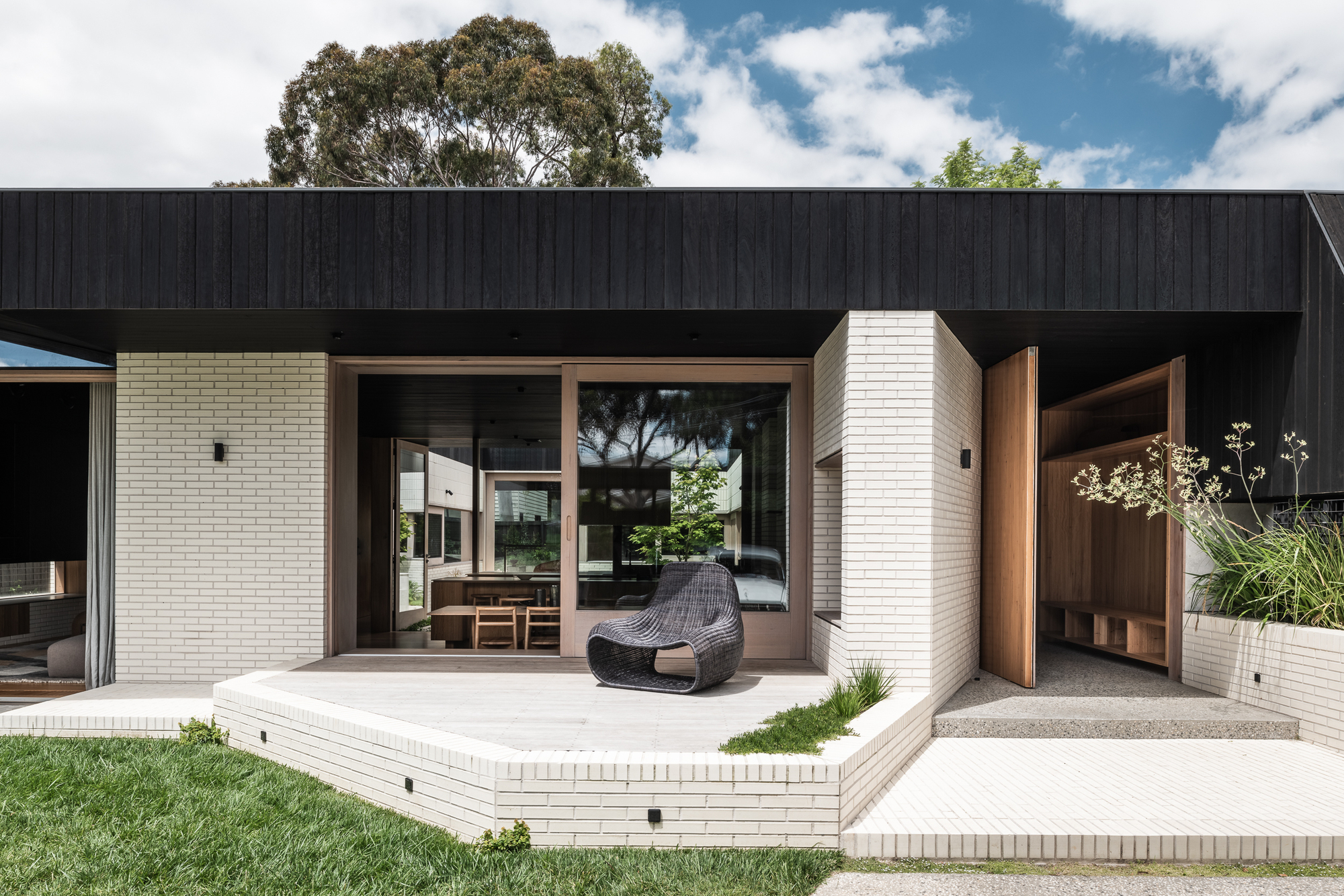 Raised concrete terrace with woven lounge chair facing glazed openings and cream brick planters