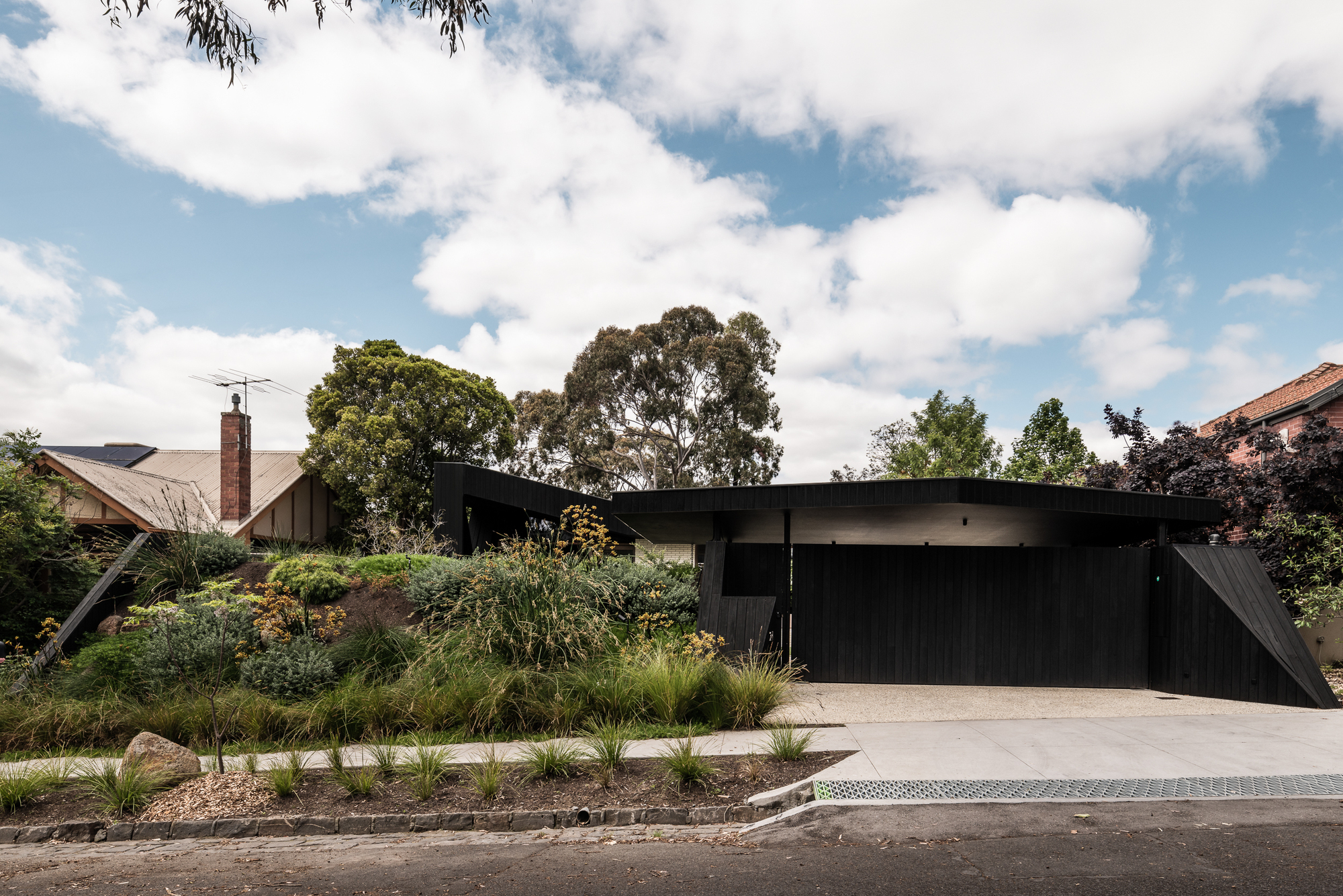 Street view of the black timber and concrete facade behind native grasses and gravel beds