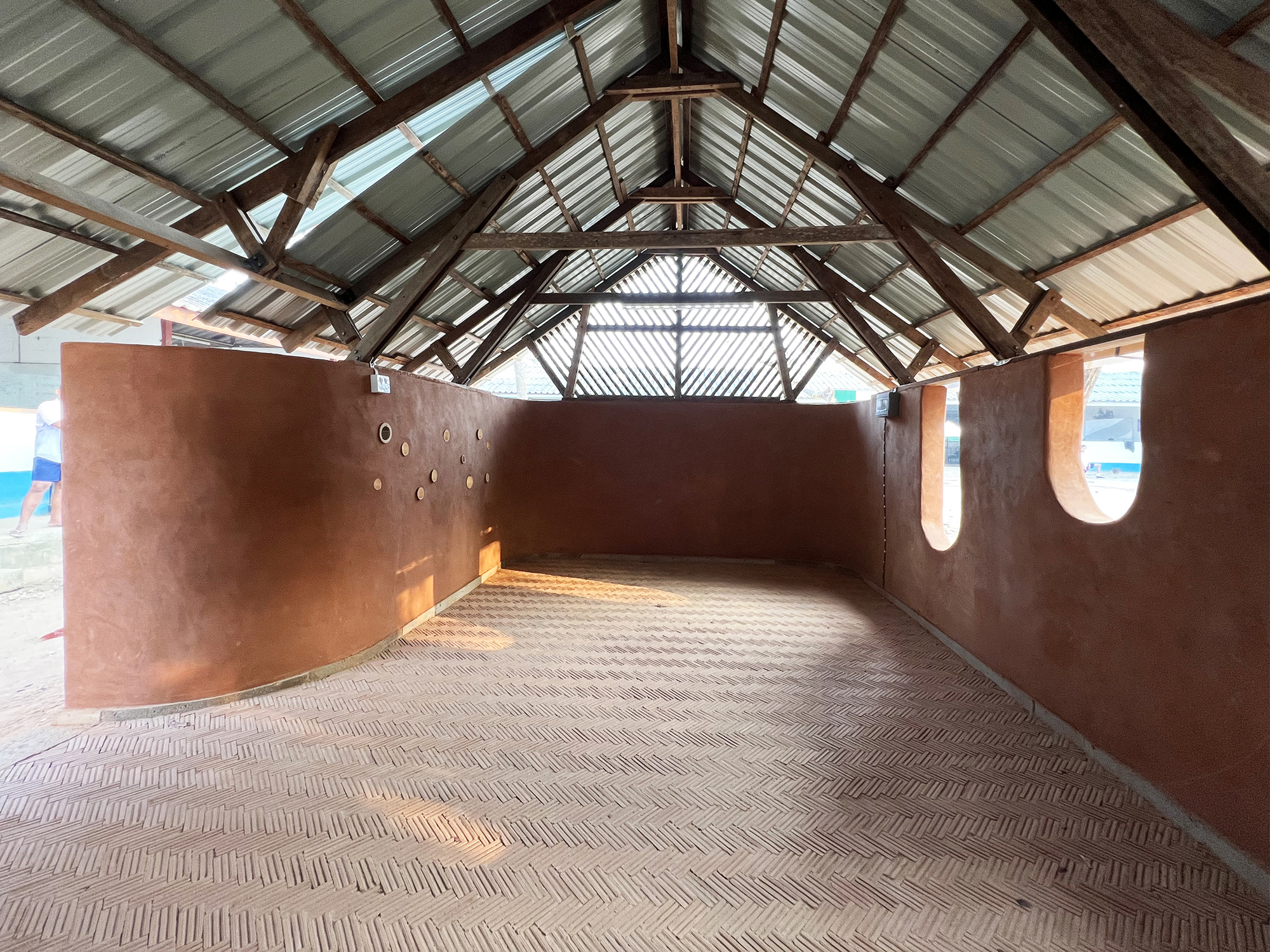 Interior of gabled space with exposed timber trusses, corrugated metal ceiling, and herringbone brick floor