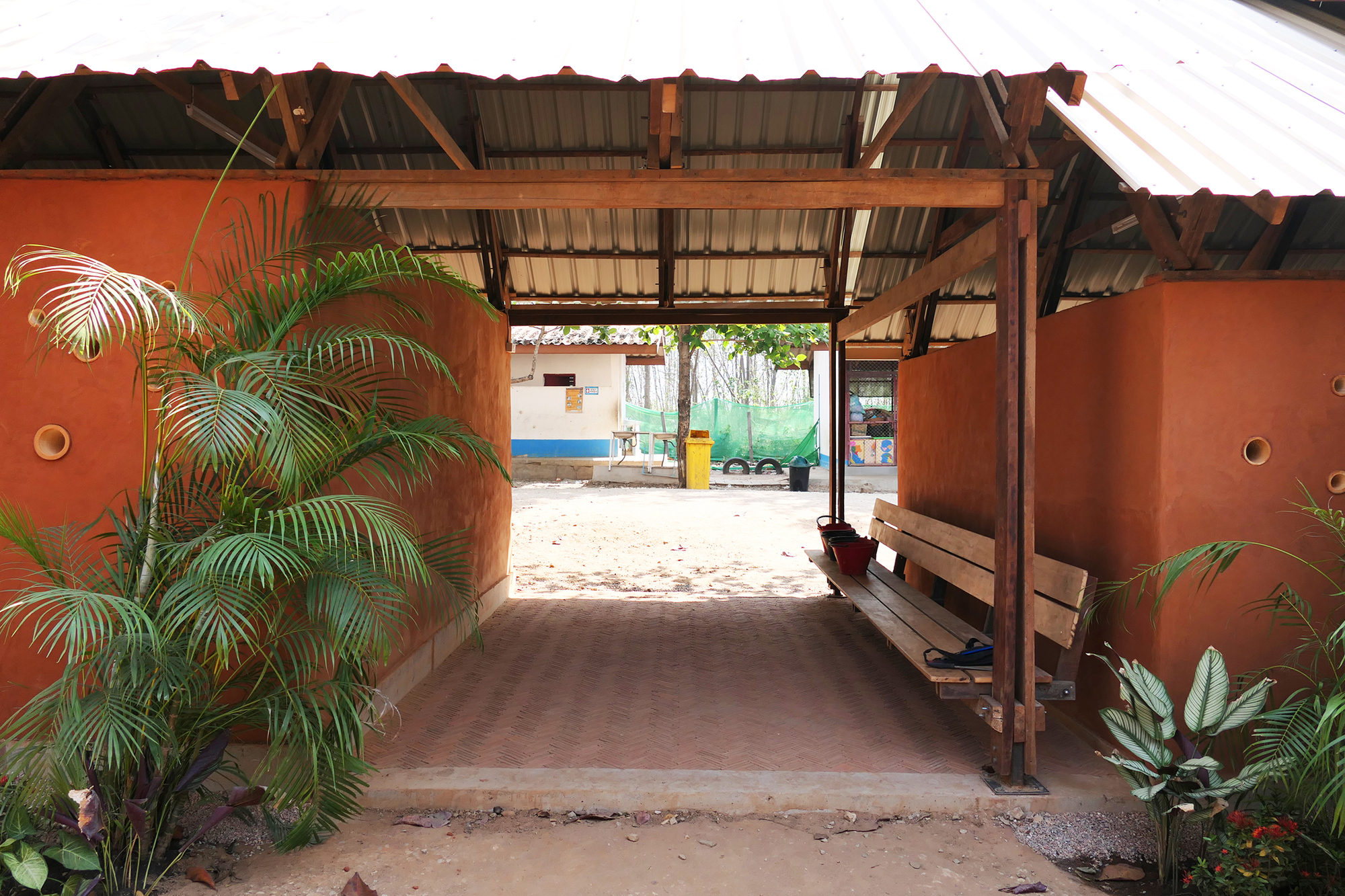 View through the gabled entry pavilion with timber post and beam structure, looking toward the compound beyond