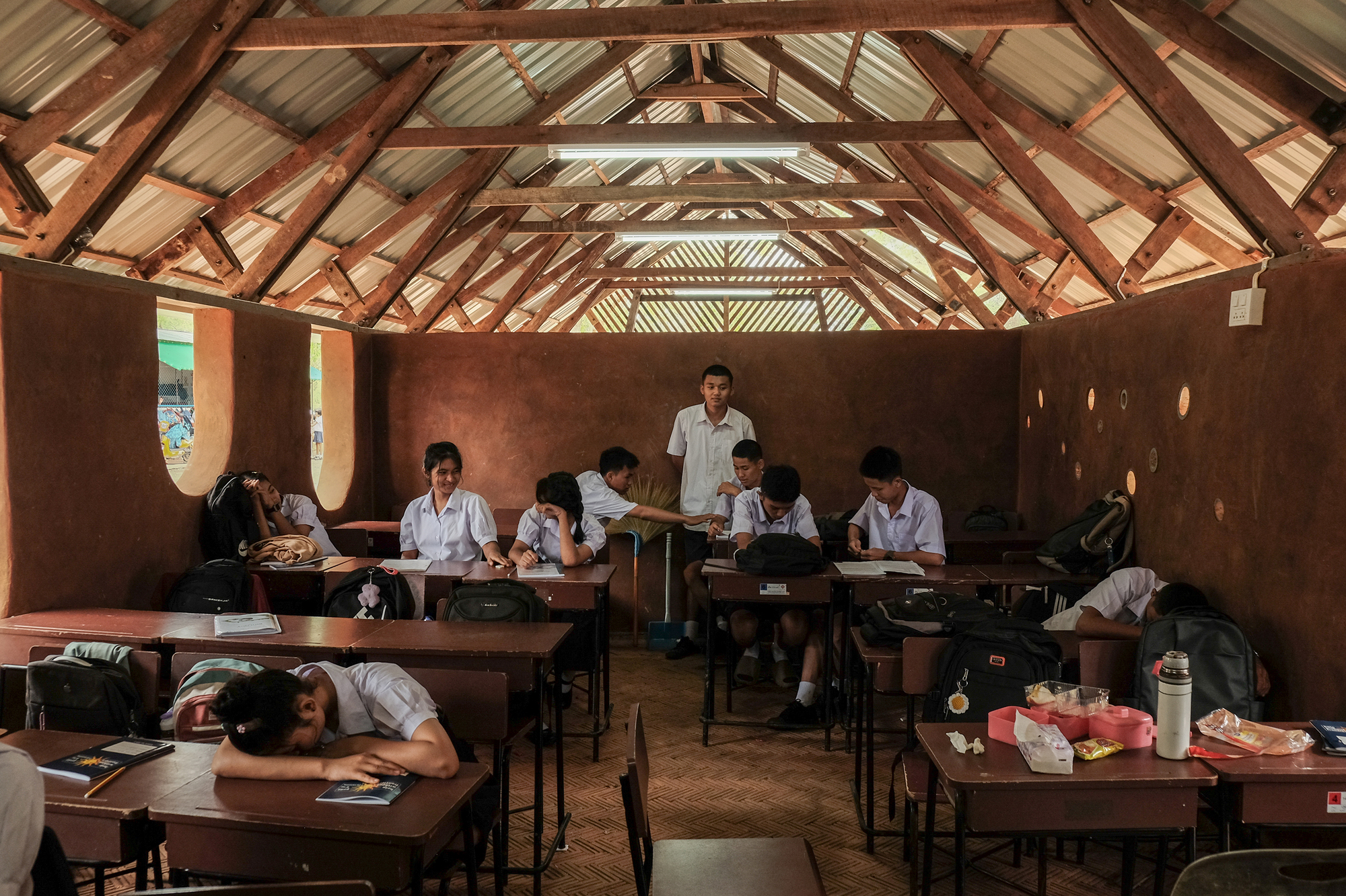 Classroom interior with exposed timber truss roof and students seated at desks beneath corrugated metal cladding
