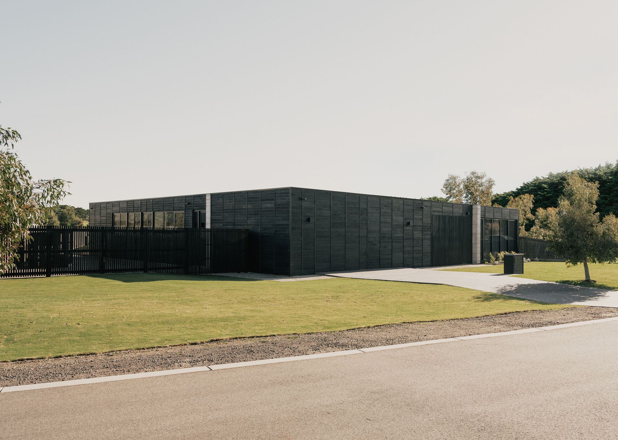 Corner view showing the charred timber cladding and vertical slat fence with trees in the background