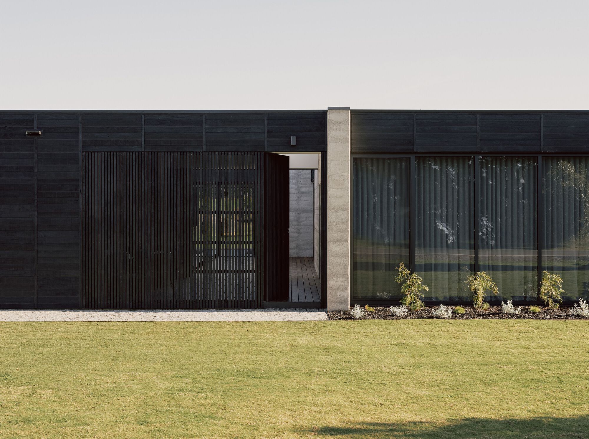 Close-up of the entry with vertical timber screen and concrete column against the dark cladding