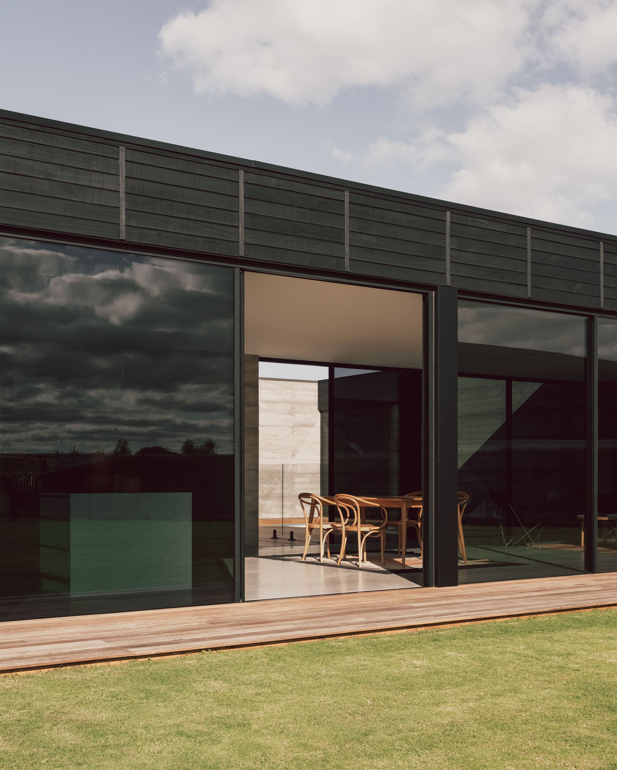 Timber deck and open sliding doors framing the dining table beneath darkening storm clouds