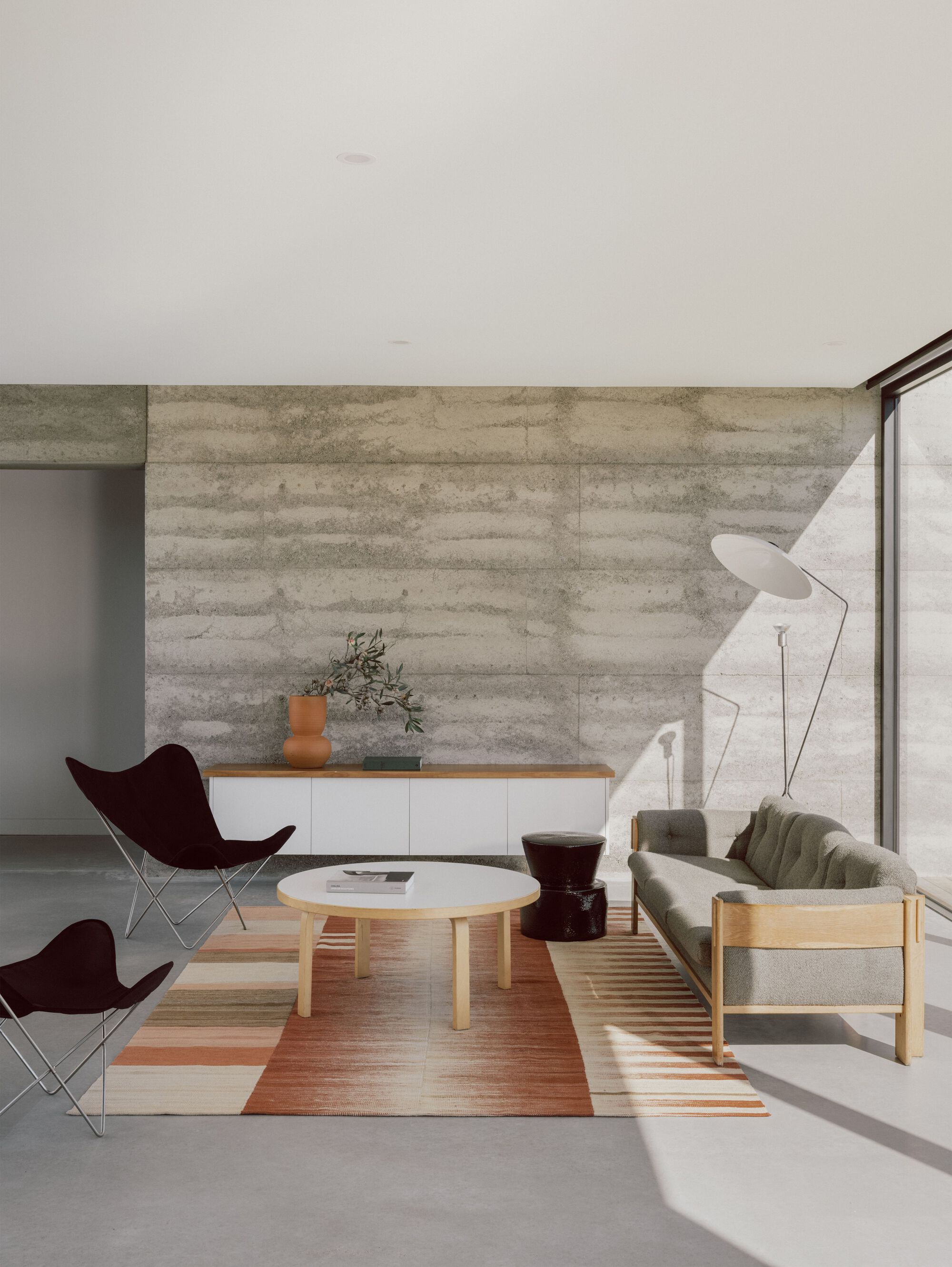 Interior view showing butterfly chairs and low table on striped rug beside boardformed concrete wall