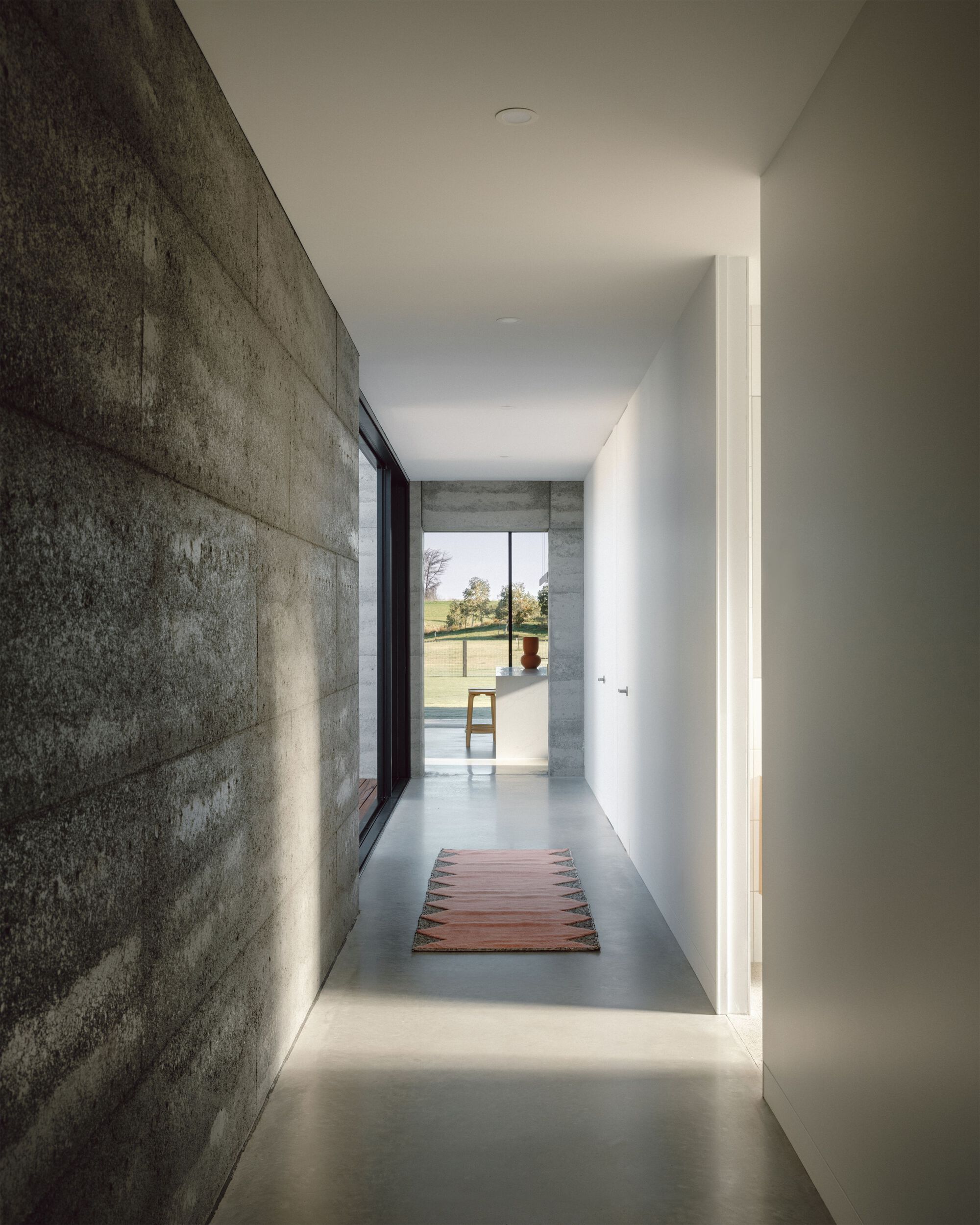 Concrete hallway with polished floor and cove lighting leading toward pool terrace in daylight