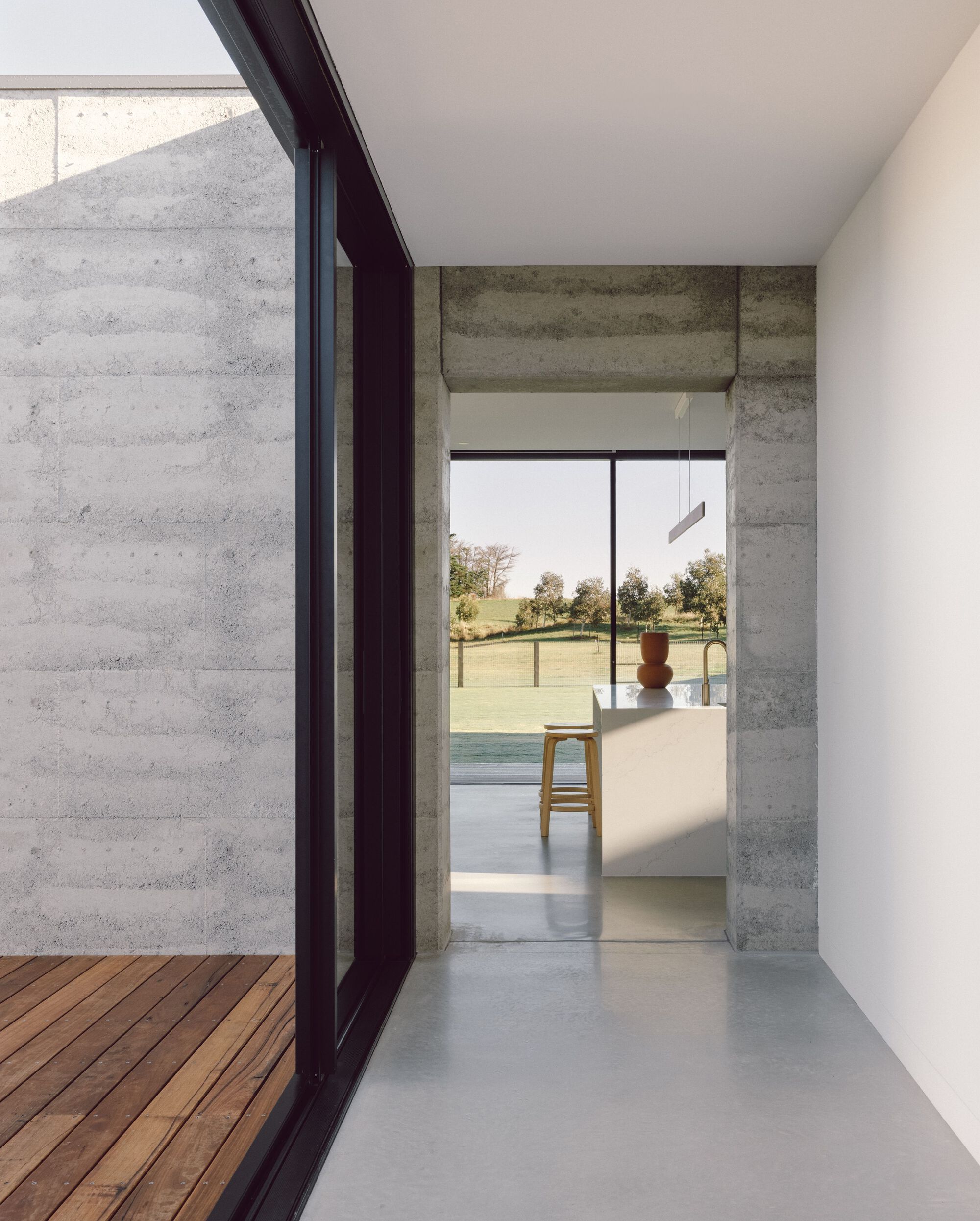 Concrete threshold opening from timber deck into interior with view toward distant landscape