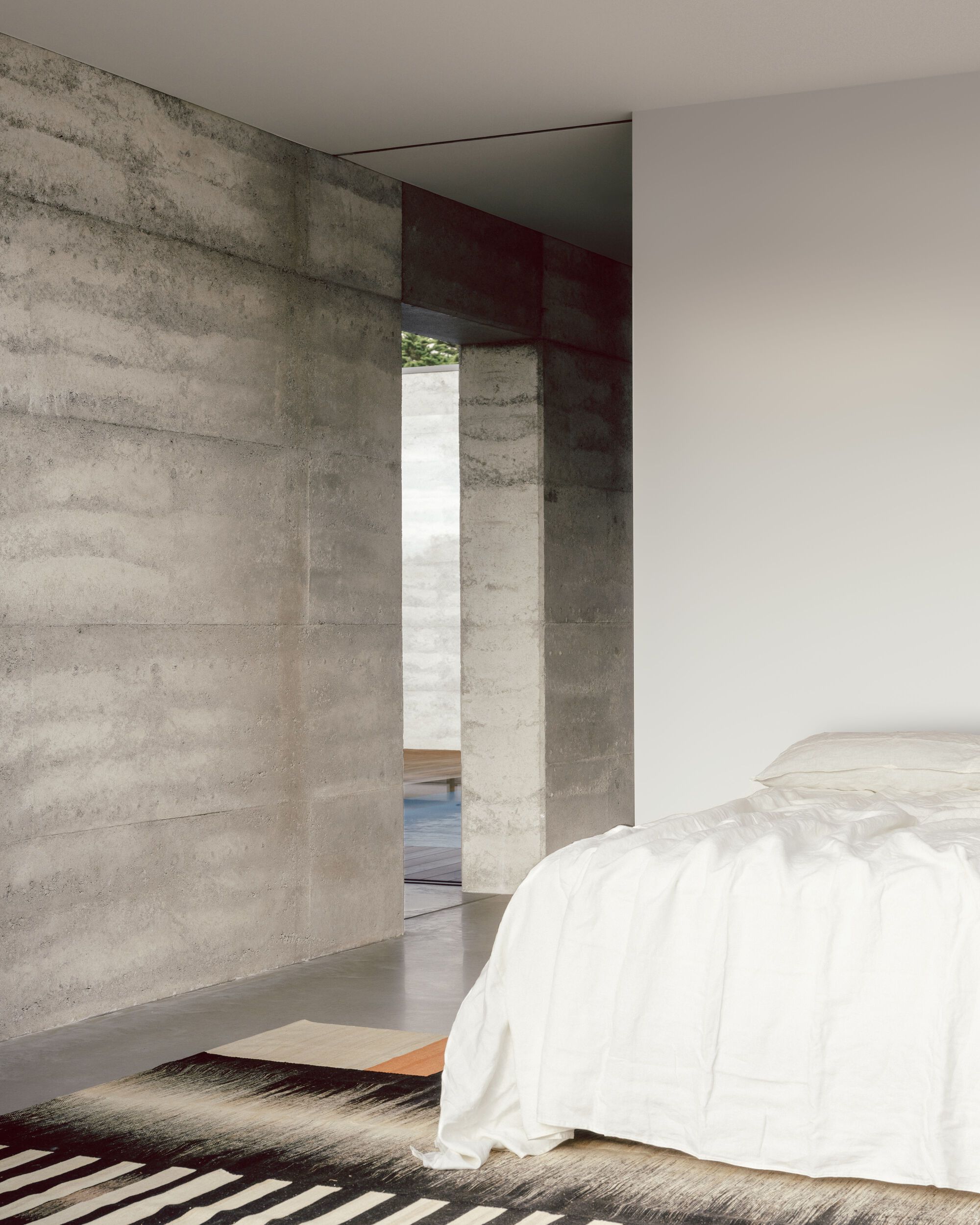 Bedroom with board-formed concrete walls and a deep red steel beam framing the doorway