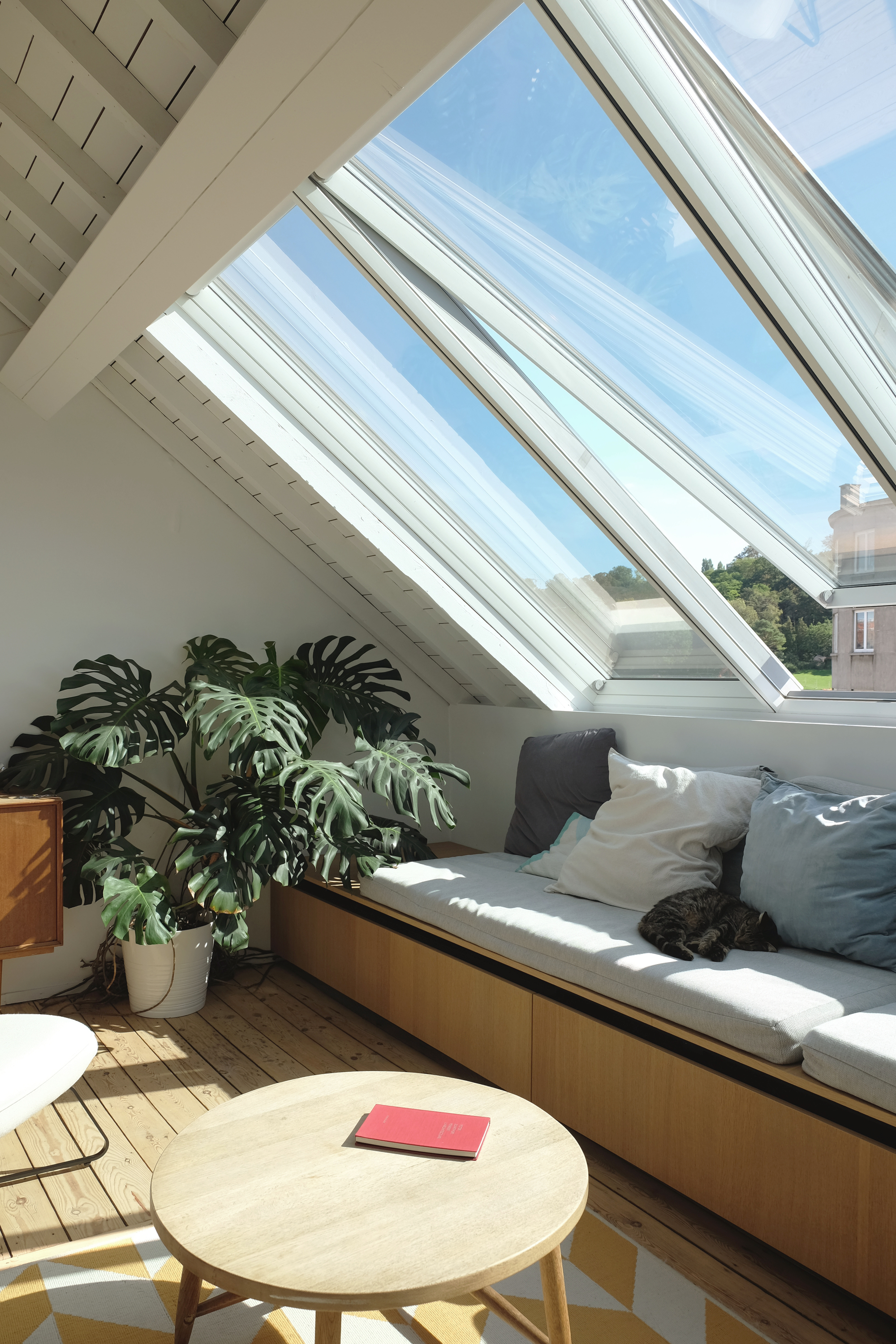 Interior view of an attic living space with angled skylights flooding sunlight onto a built-in bench