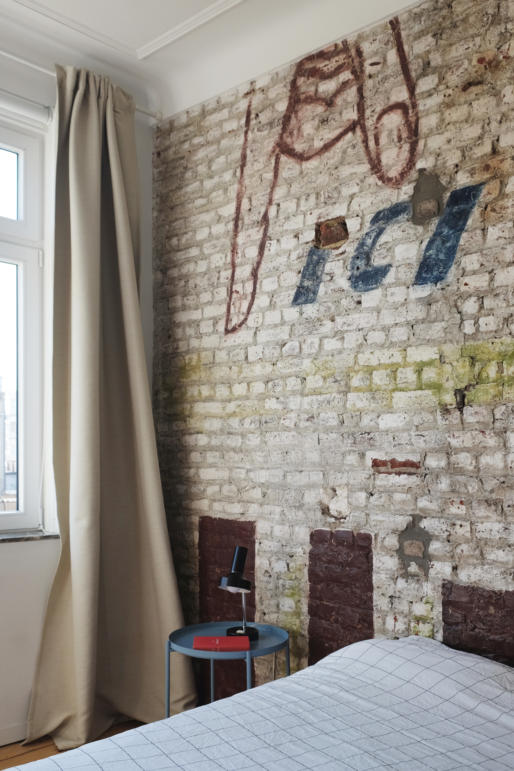 Exposed whitewashed brick wall with faded painted signage in a bedroom corner with draped curtains