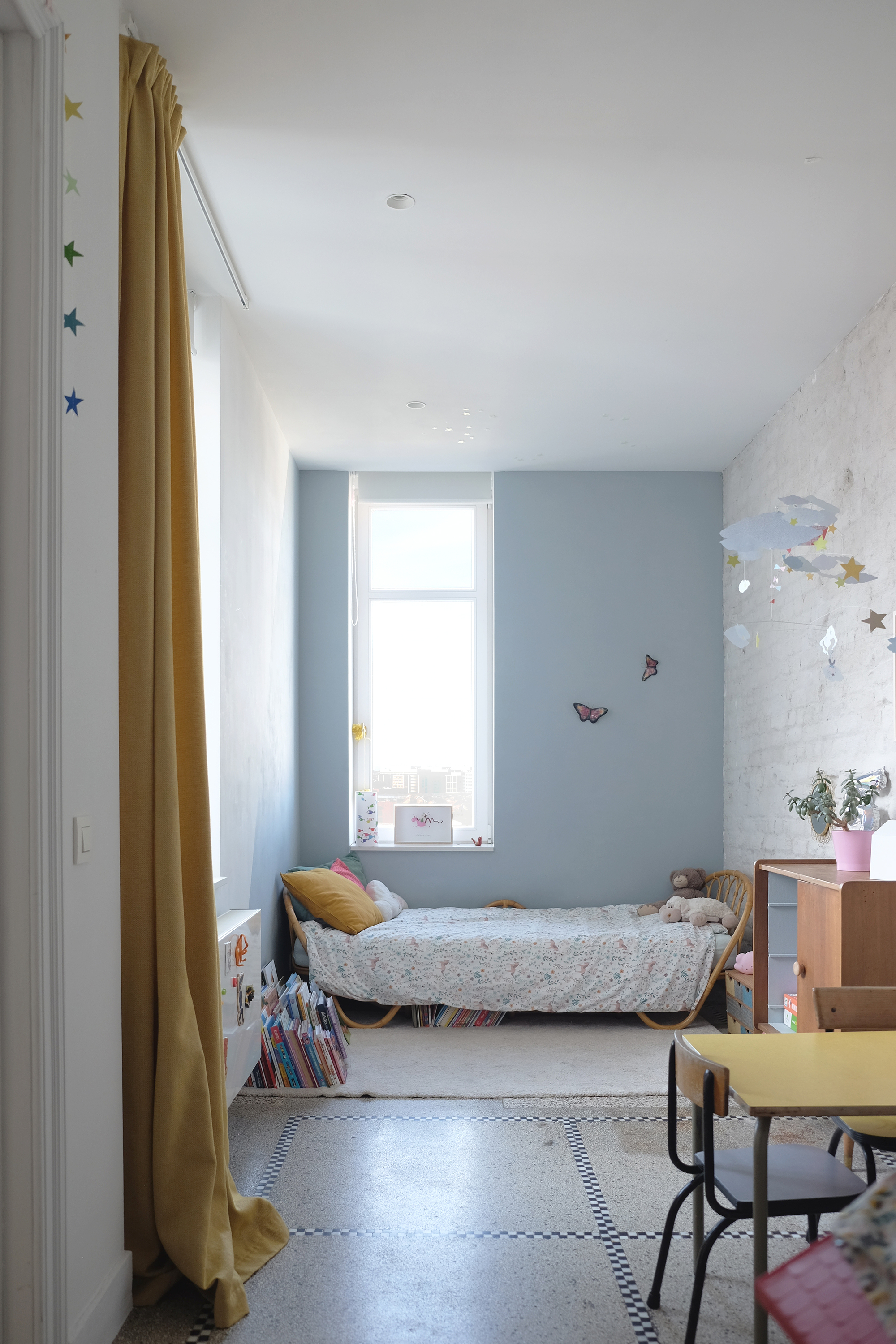 Narrow bedroom with blue accent wall and terrazzo flooring divided by yellow curtain