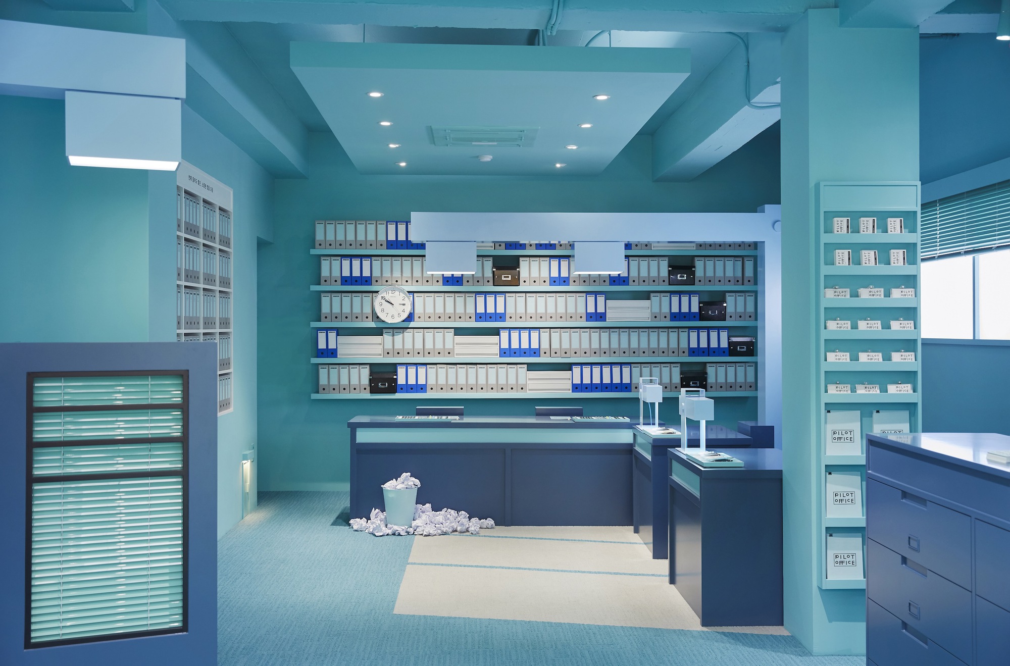 Office interior with turquoise walls, navy service counters, and filing binders on shelves under recessed lighting
