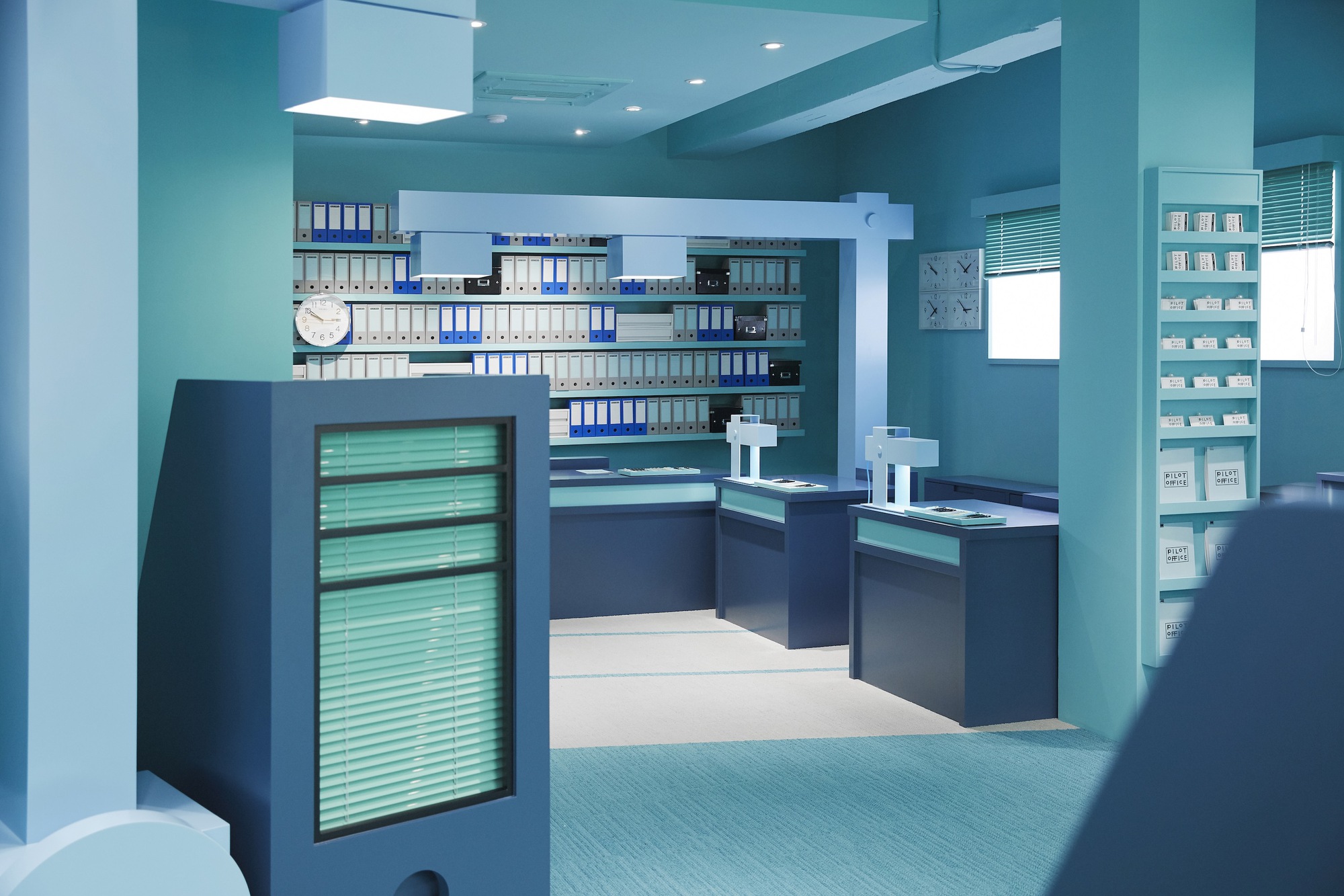 View through columns showing navy workstations with illuminated panels against turquoise walls and blue carpet