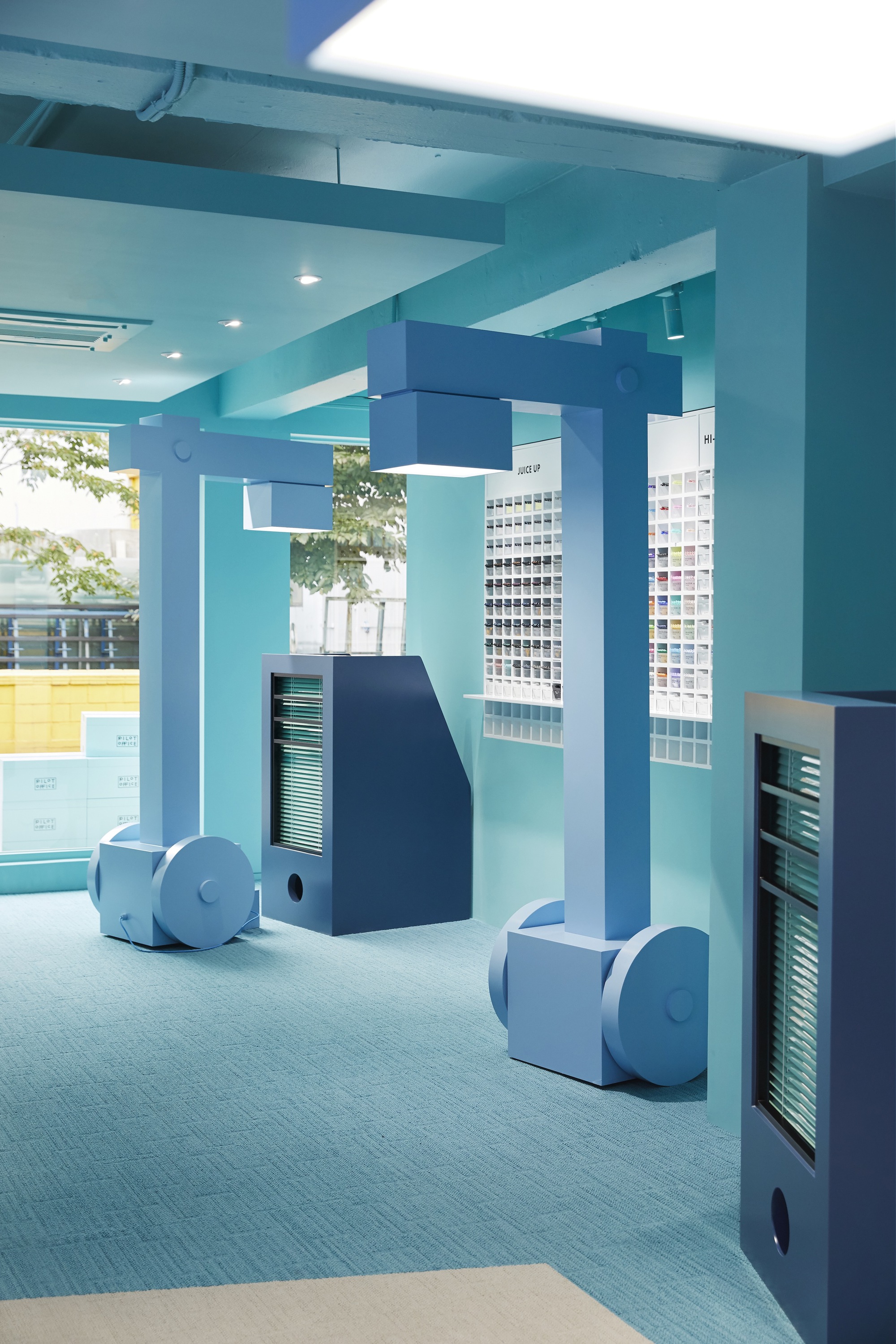 Interior corridor with square columns and curved blue storage forms on the floor near glazed openings