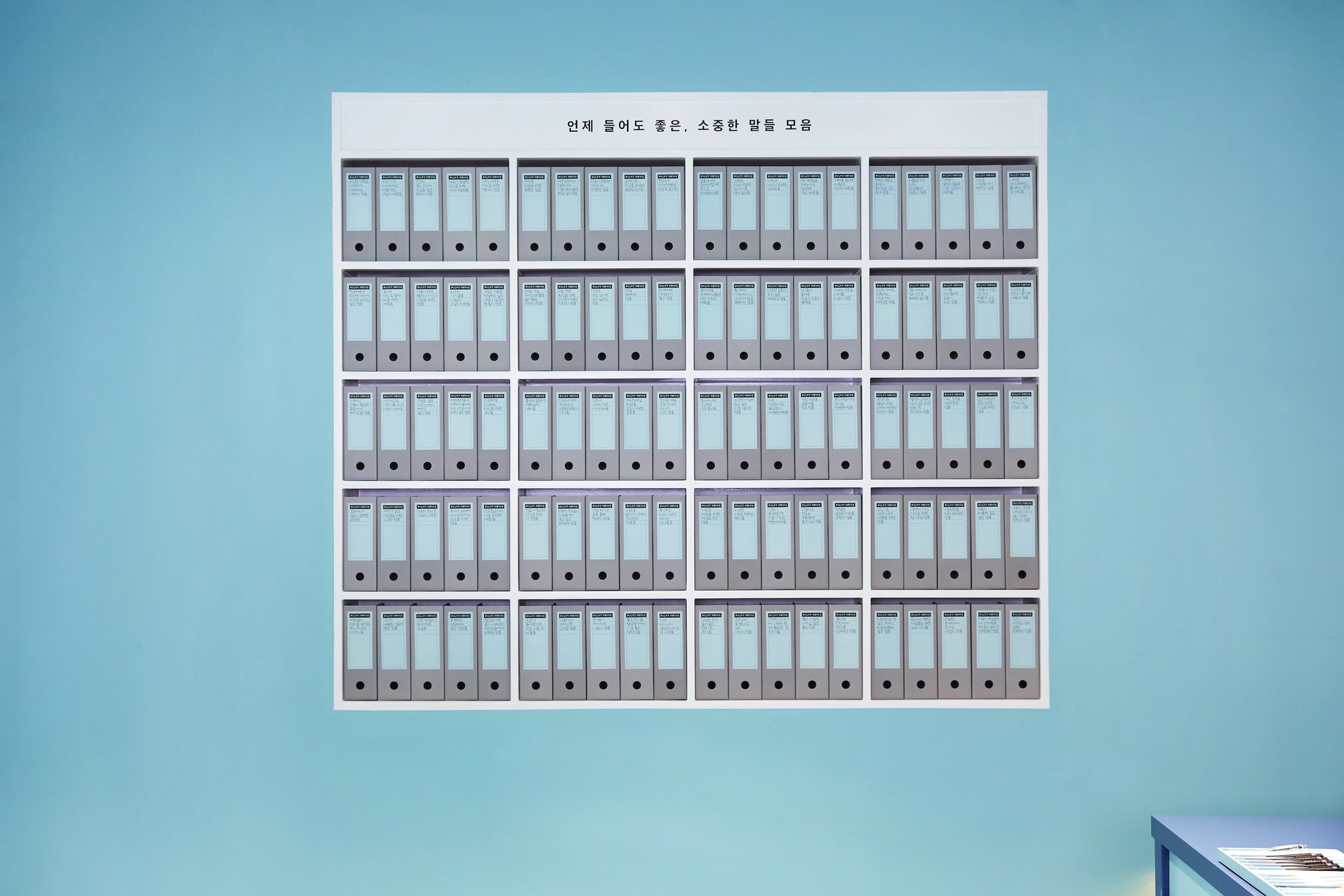 Wall-mounted grid of labeled binder boxes arranged in five rows against a teal surface
