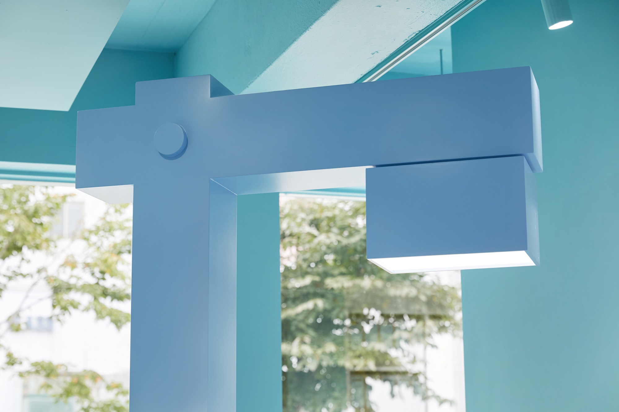 Articulated pale blue display mount with cylindrical joint viewed through glass with trees beyond