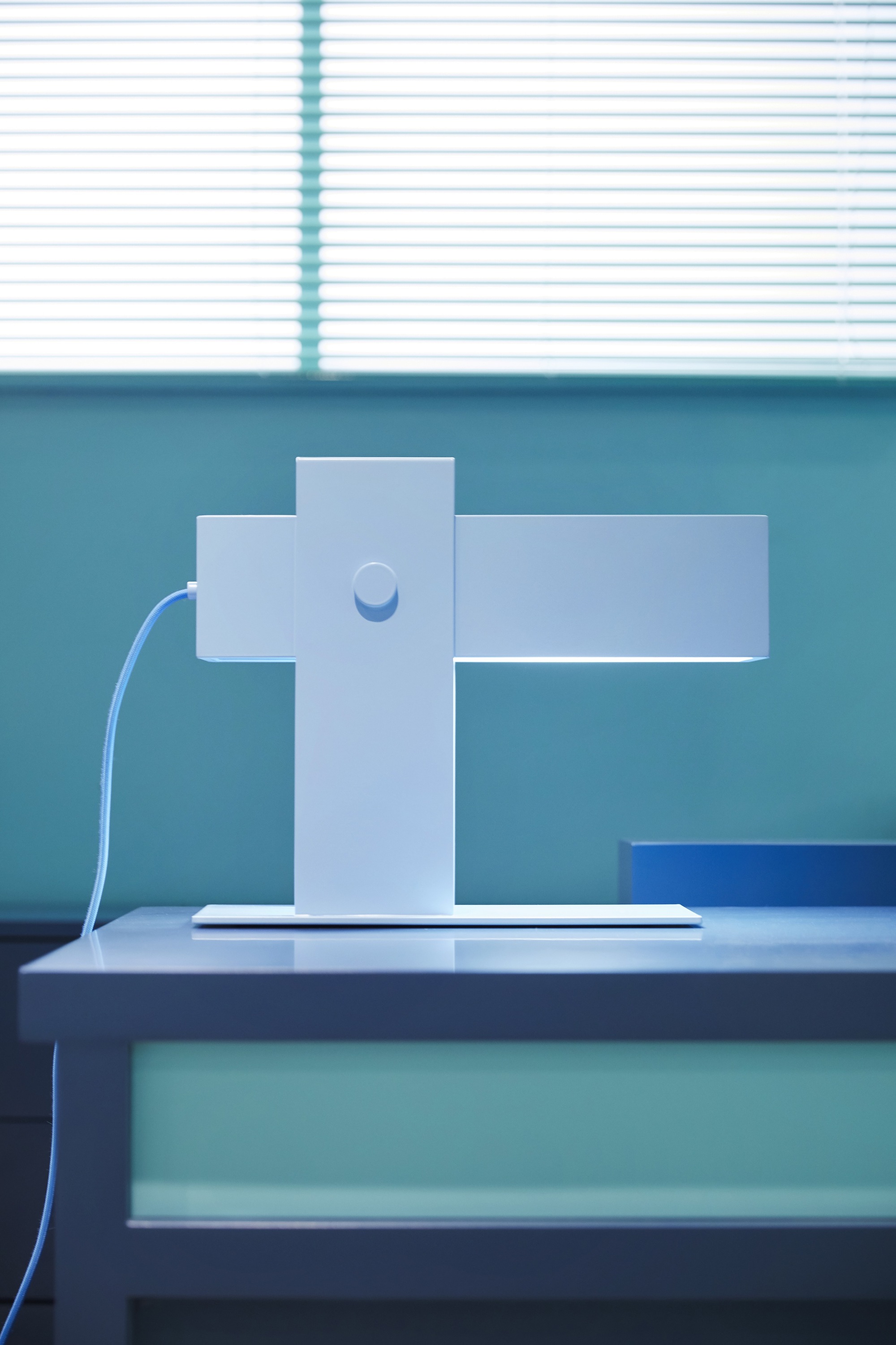 White cross-shaped display stand on a platform with venetian blind shadow above