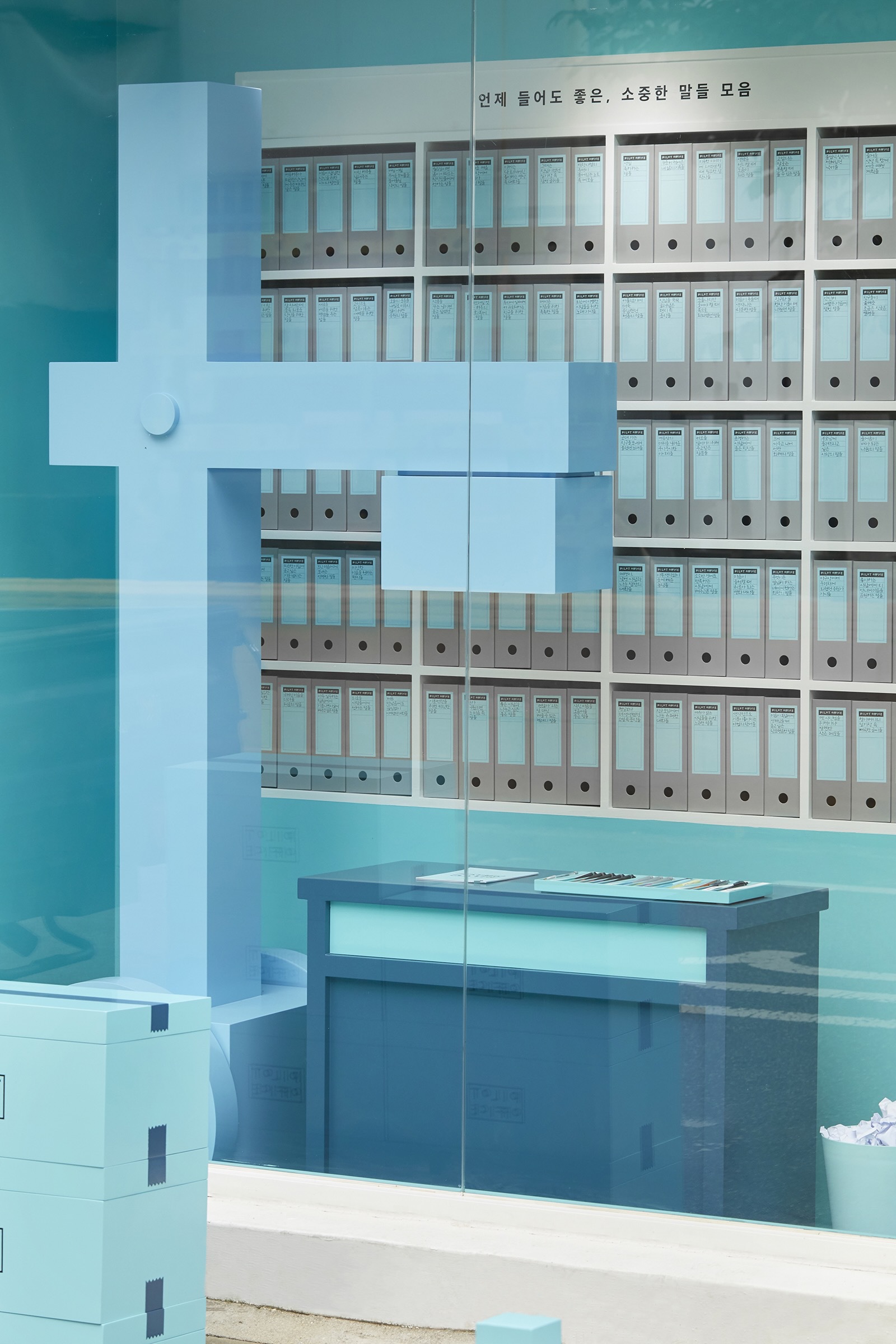 Glass partition reflecting rows of white binders on wall-mounted shelving with a low bench