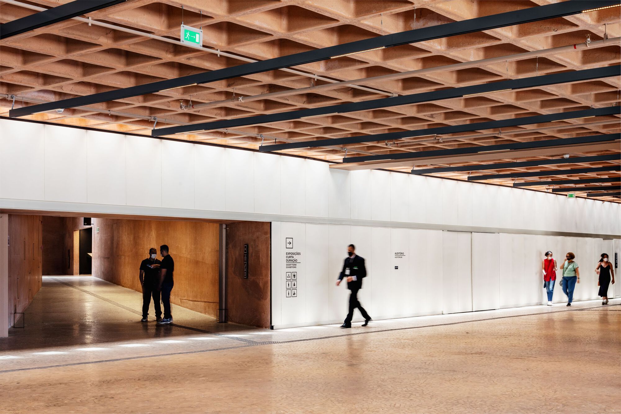 Corridor with timber waffle ceiling, white walls, and visitors walking along the passage