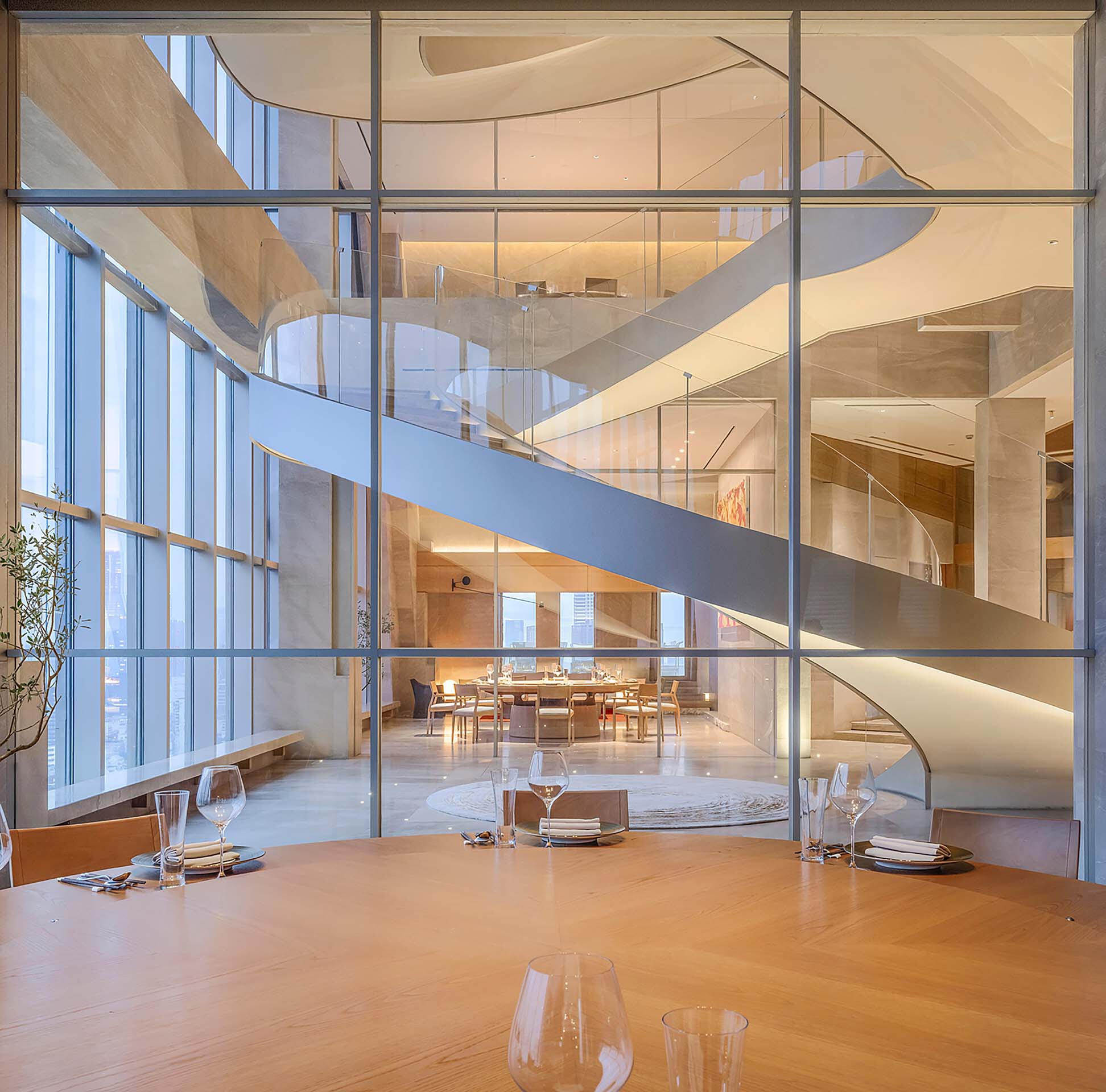 View through steel-framed glass partition of spiraling white staircases connecting multiple dining floors