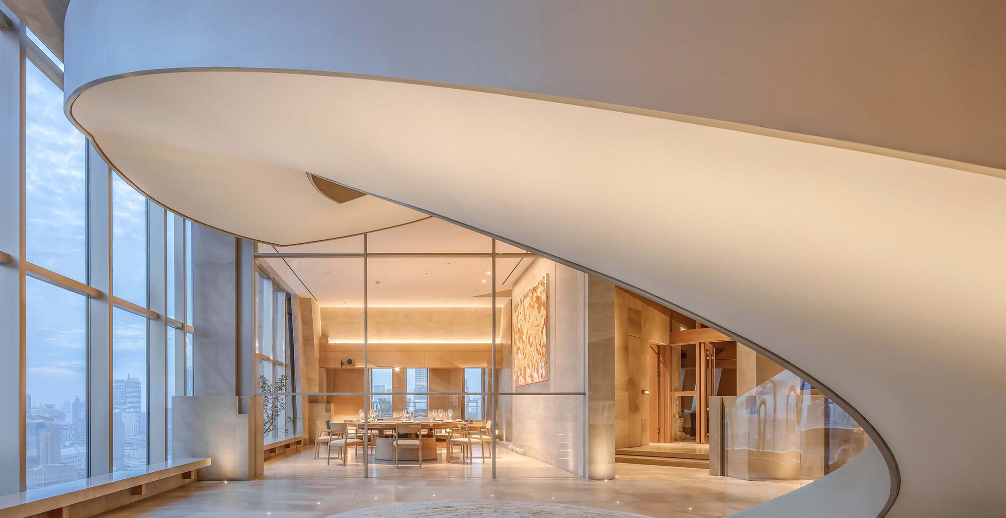 Curved white staircase with underside view showing smooth soffit beside tall curtain wall glazing