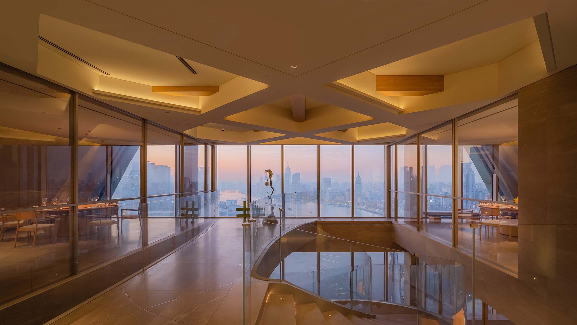Curved stair landing with polished floor reflecting a figure walking past panoramic windows at sunset