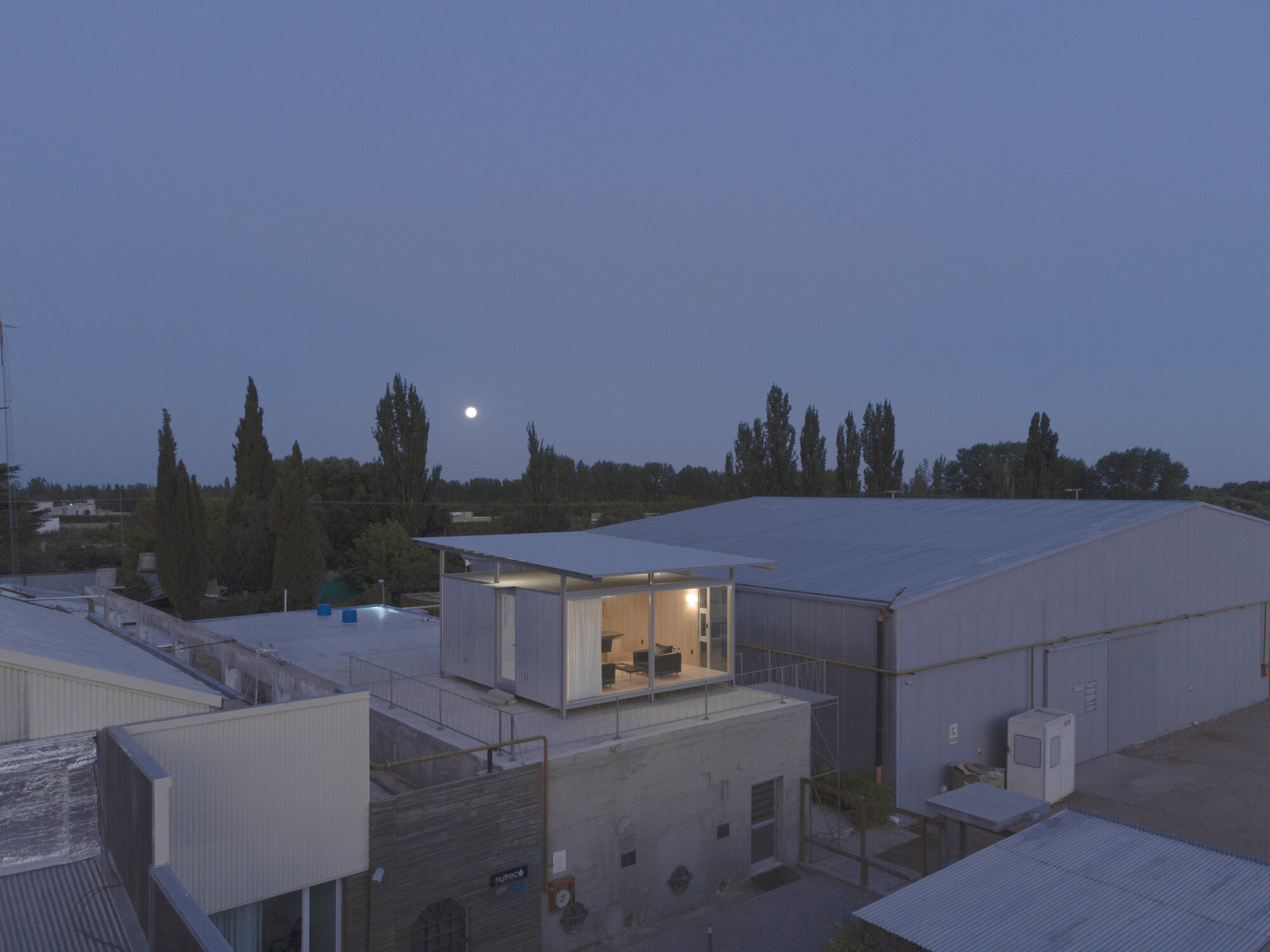 Elevated rooftop pavilion with glass walls and timber cladding at dusk with moon rising
