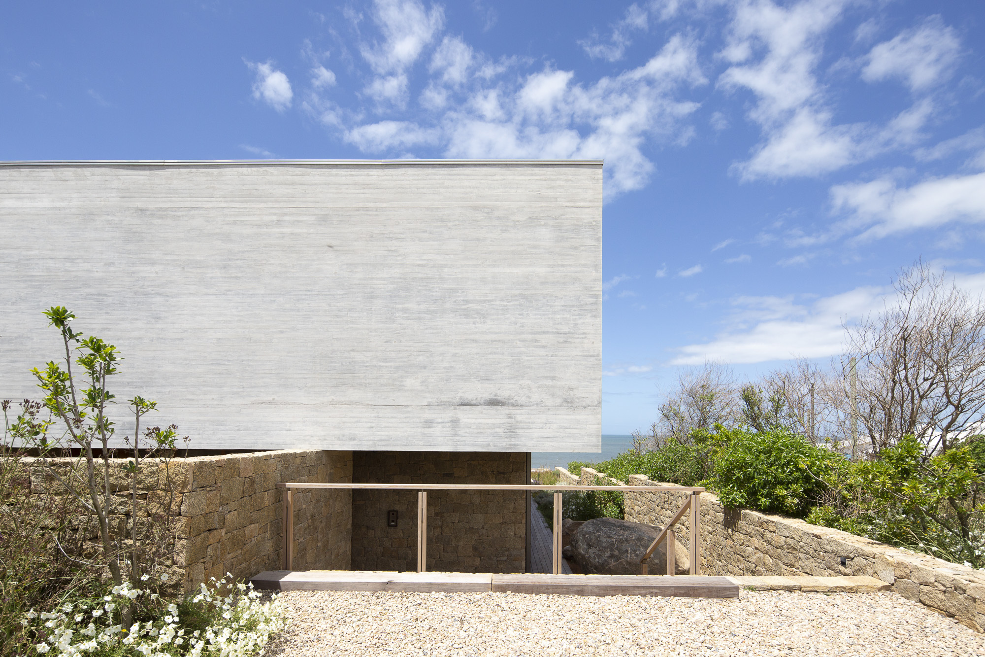 Concrete upper volume cantilevered above a recessed stone base with distant ocean views