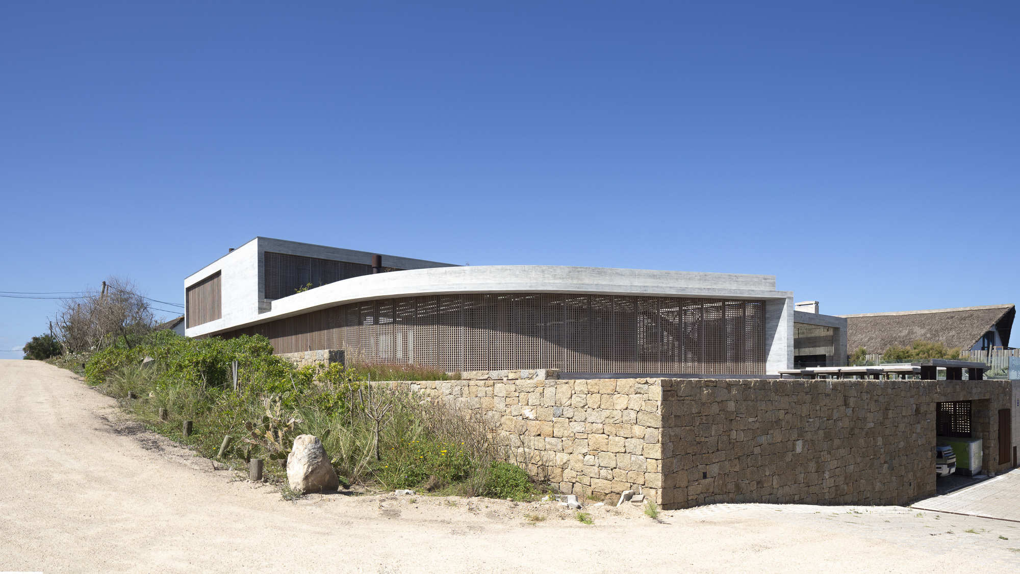 Street view of the stone base wall topped by timber lattice screen and concrete roof canopy