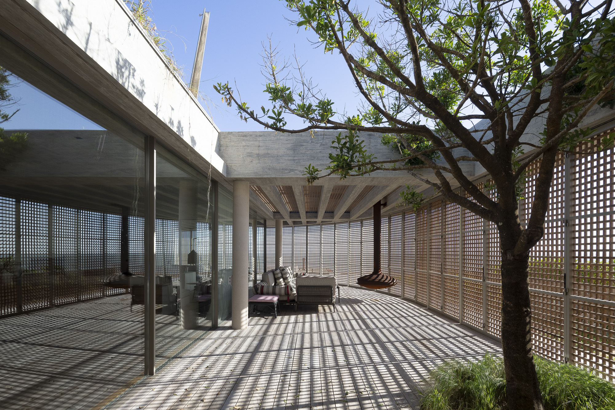 Covered terrace with timber lattice screens casting shadow patterns on the deck beside a planted tree