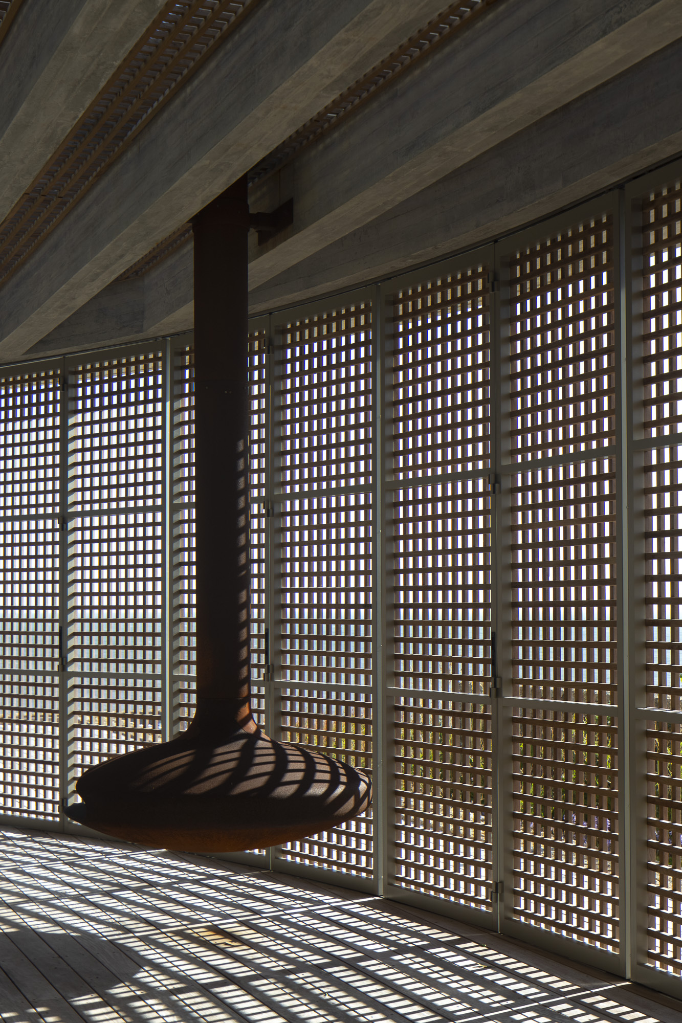 Corner view of the timber lattice wall filtering light onto a suspended daybed beneath exposed concrete beams
